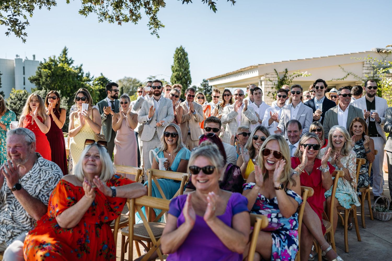 Wedding guests celebrate with raised arms during outdoor reception.