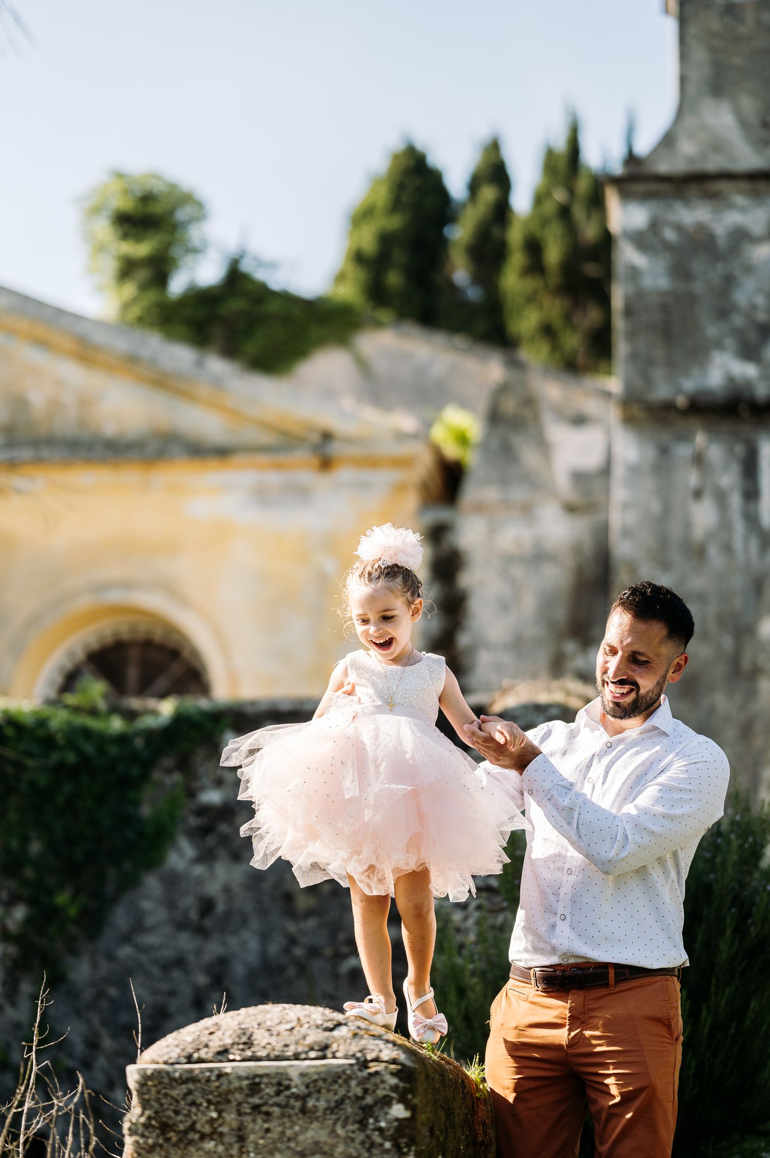 Playful moments captured in a garden setting with a pink tulle dress against stone walls.
