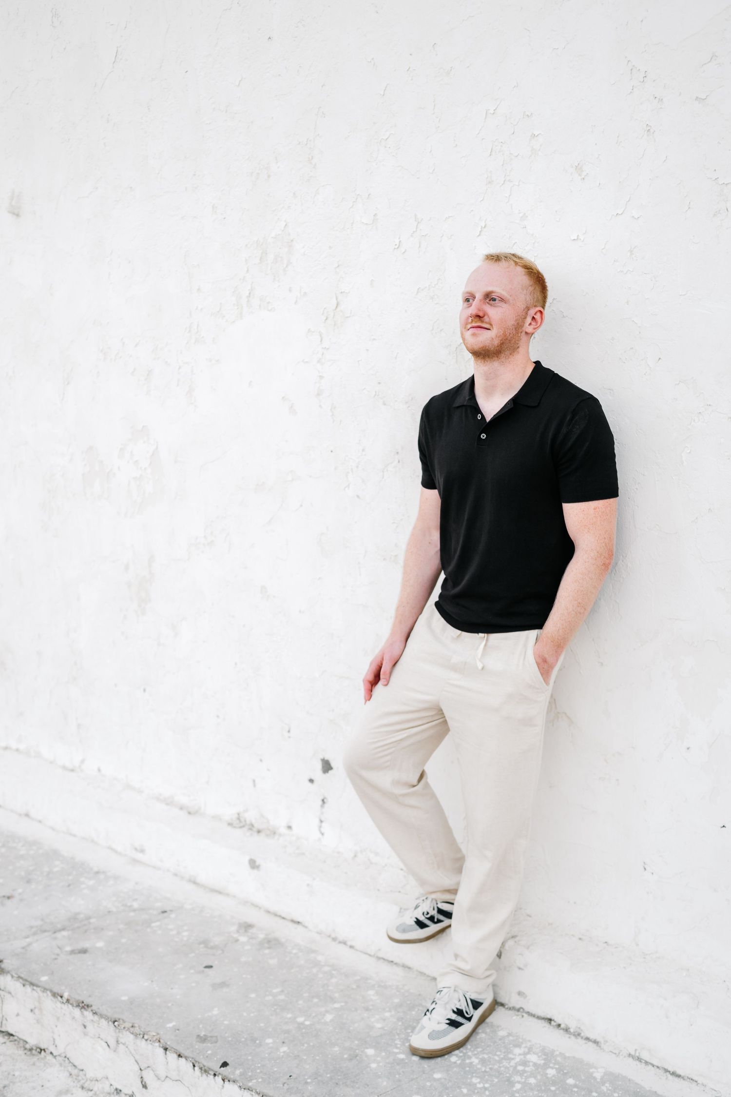 Man in black polo and khaki pants posing against white wall.