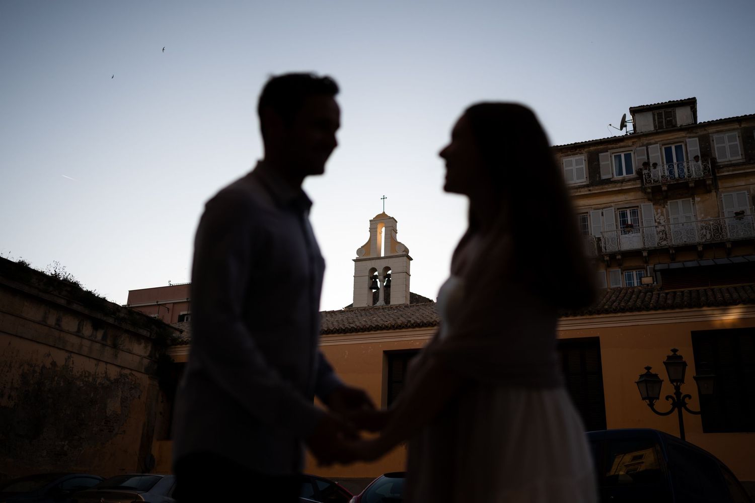 Silhouettes of a couple against a sunset sky with architectural elements.