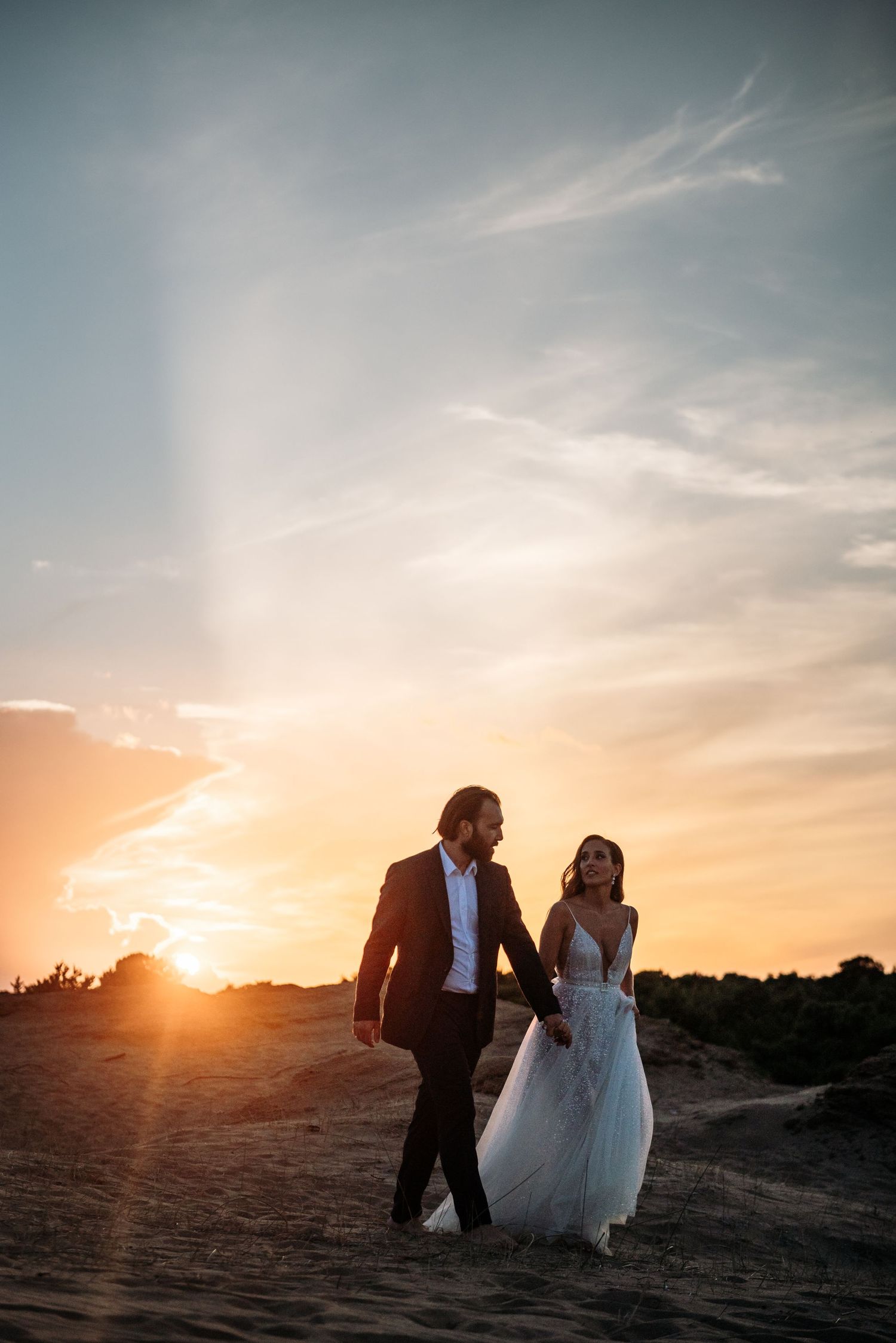 Wedding couple walks along sandy path during golden hour sunset.