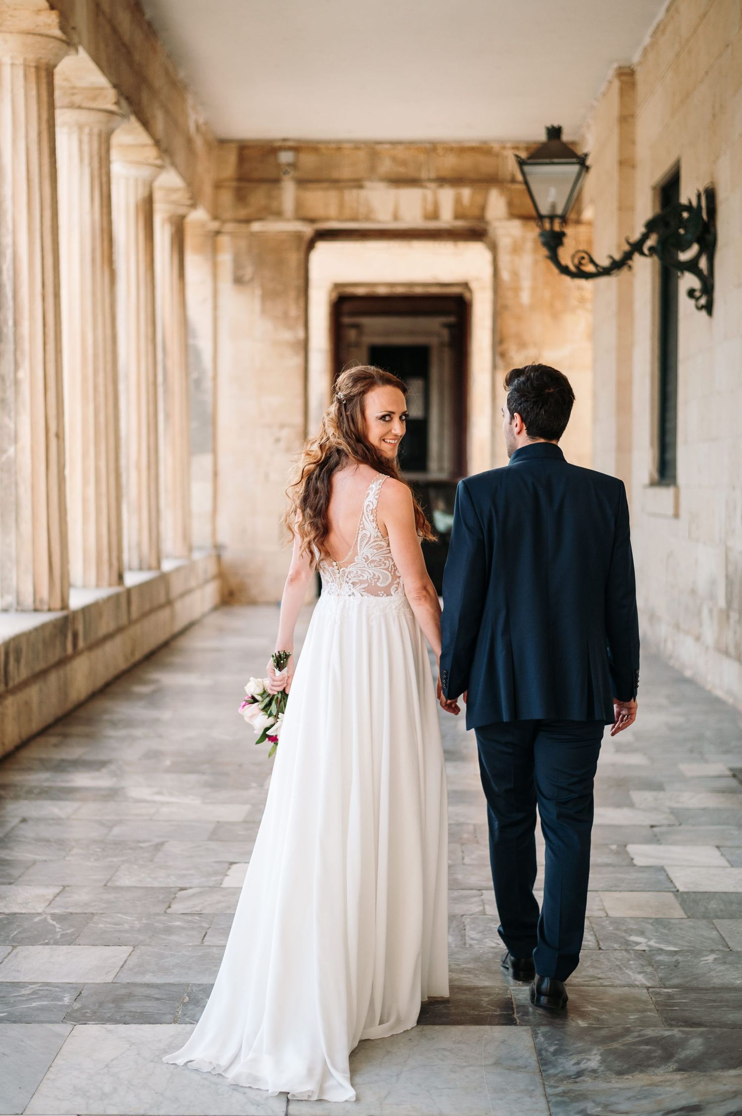 Couple walking through historic stone colonnade during romantic wedding photo session.