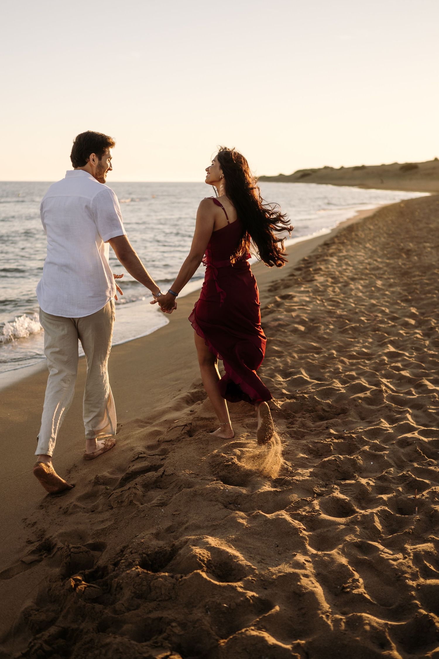 Couple walking hand in hand on a beach with dramatic sunset lighting.