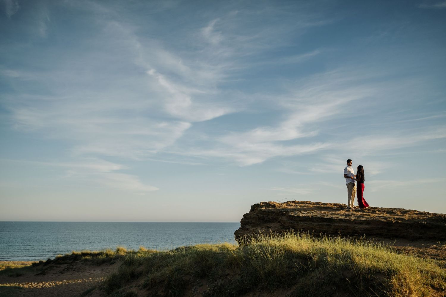 Panoramic view of a coastal cliff with a couple silhouetted against the sky.