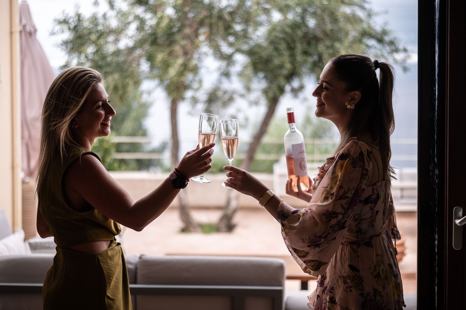 Silhouettes toast champagne glasses by window during wedding preparations.