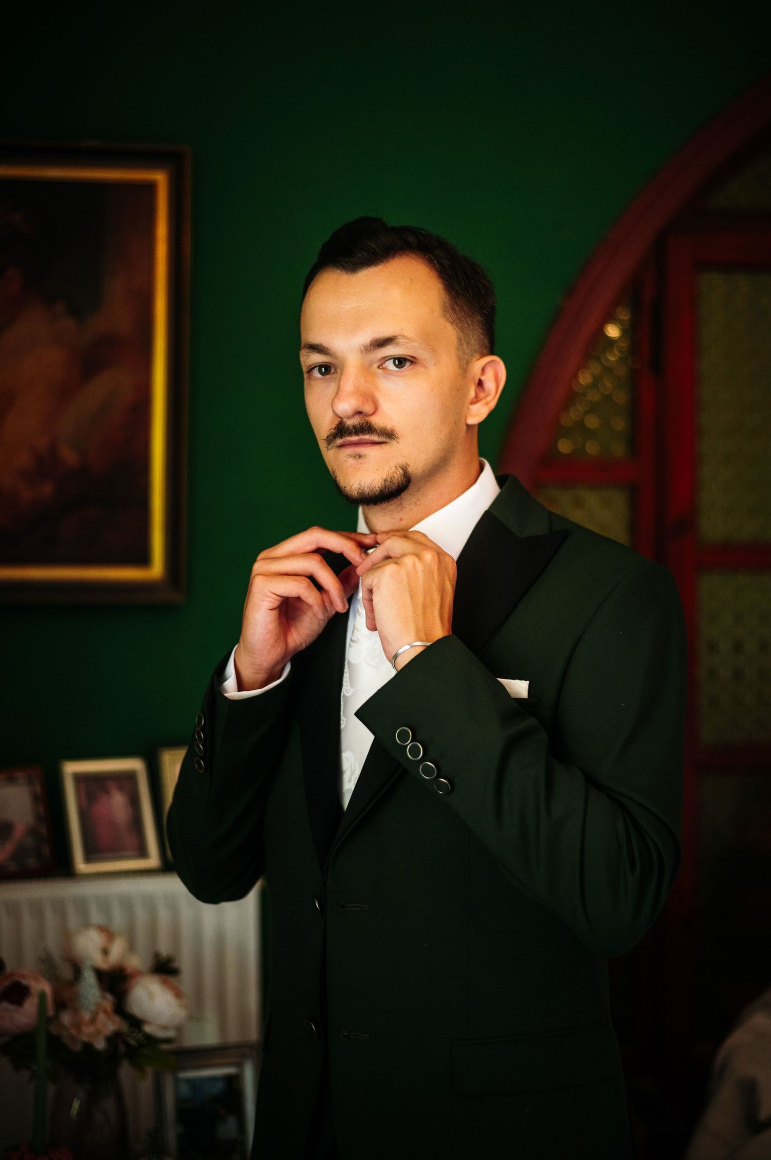 Dramatic lighting captures a groom in a black suit against a dark green background.