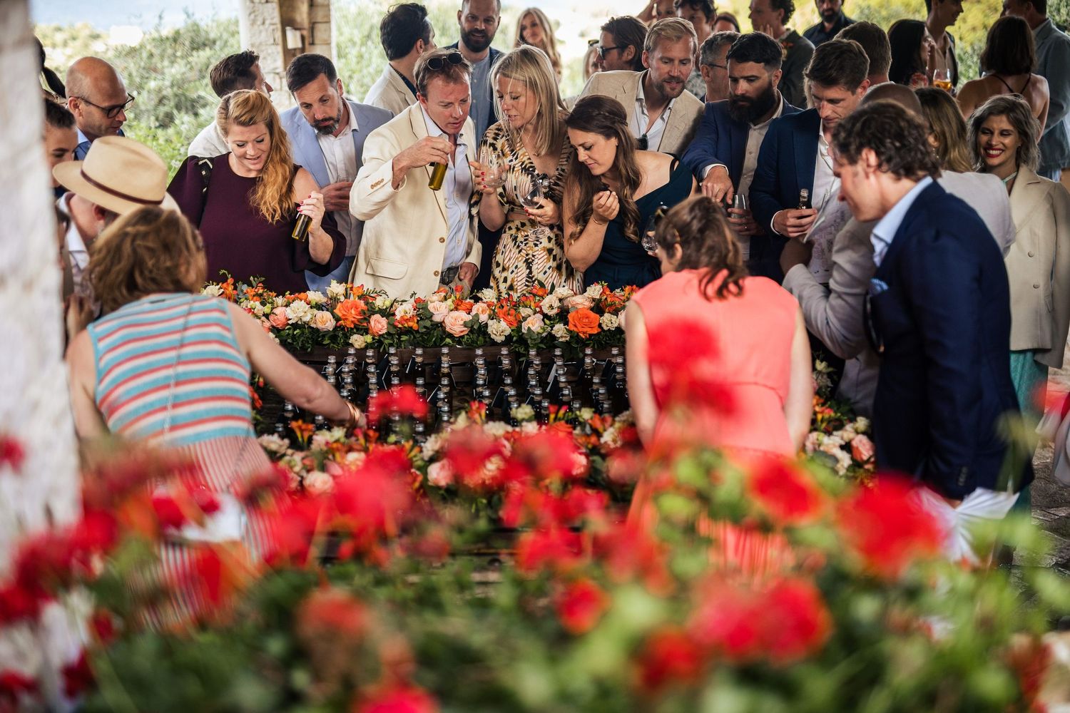 Wedding guests gathered around a bar with red flowers in the foreground.