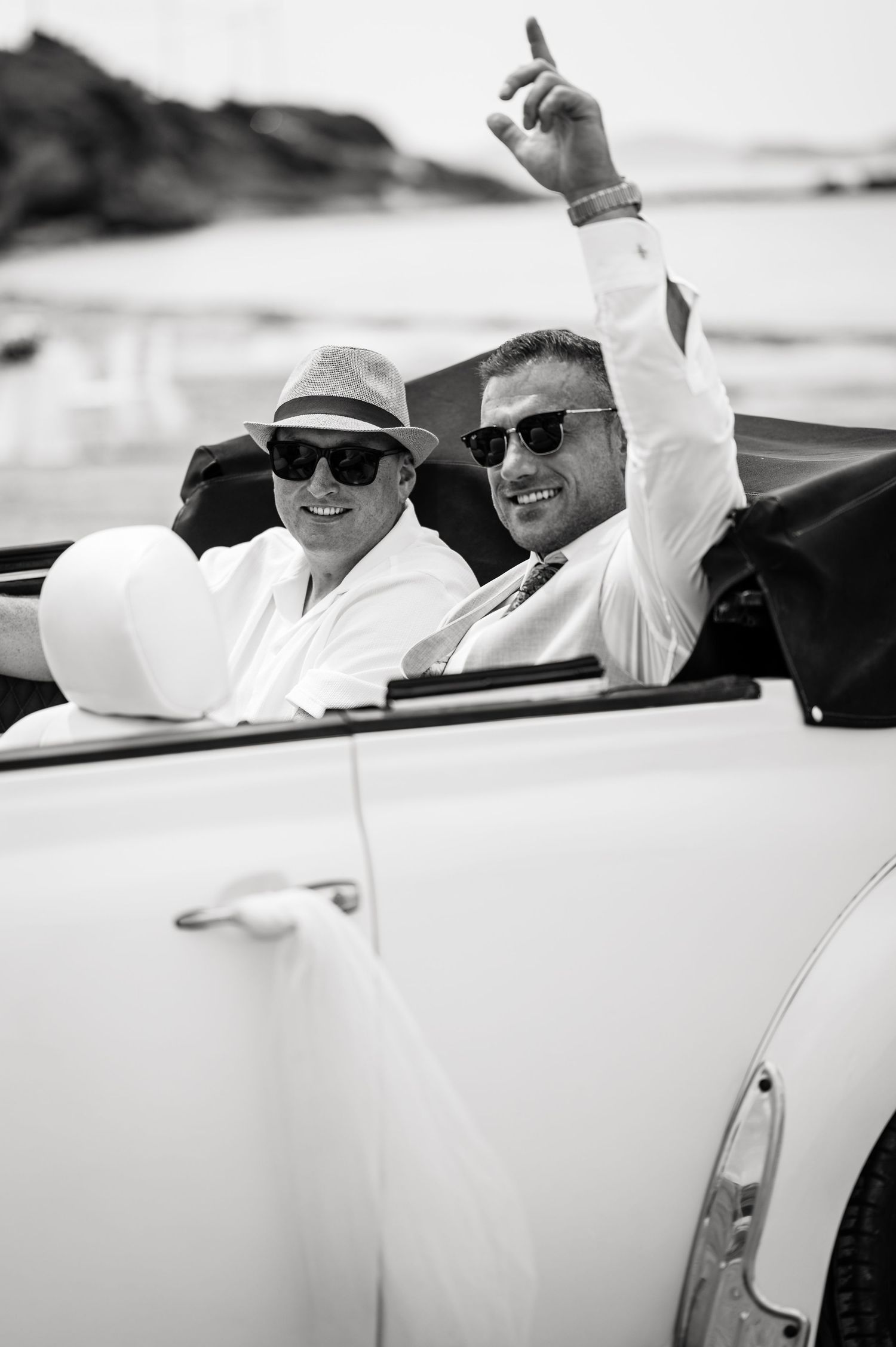 Black and white photo of guests riding in a classic convertible car.