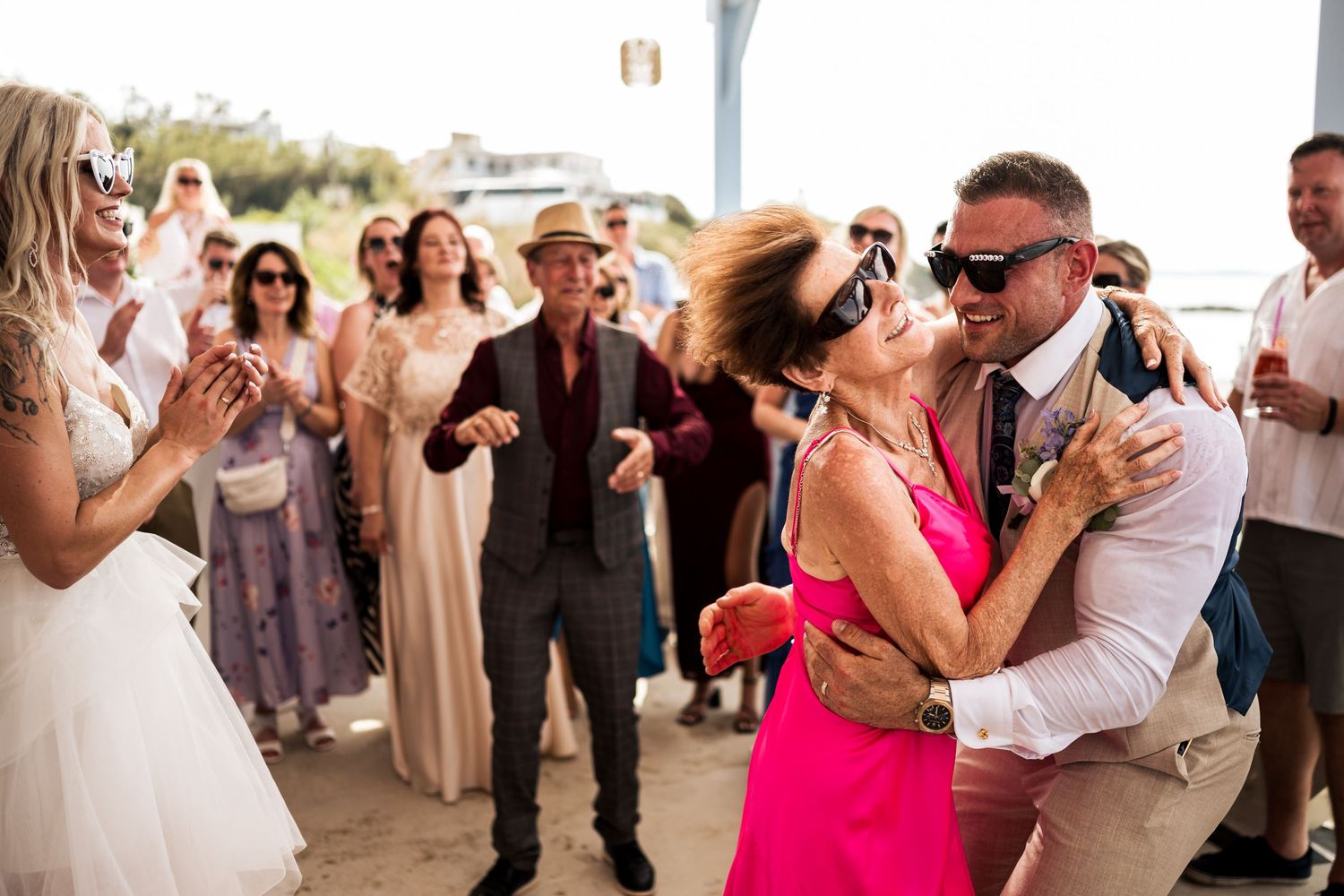 Lively beach wedding reception with guests dancing and celebrating in casual summer attire.