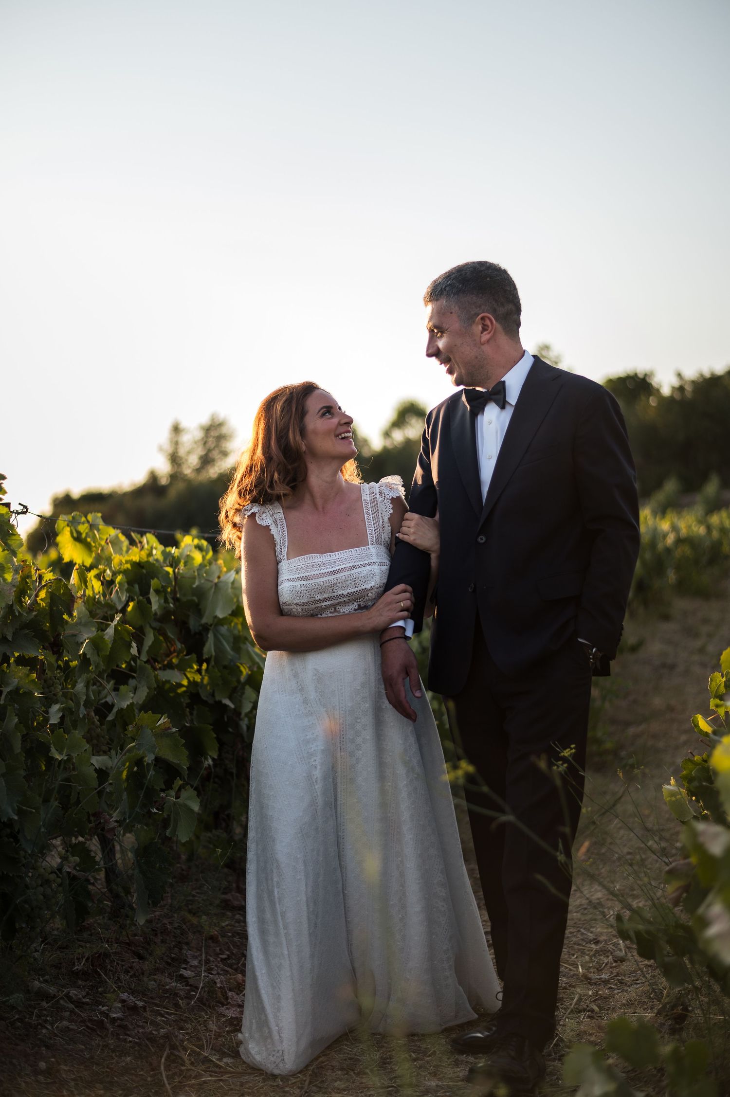 Couple walking through vineyard rows during sunset wedding photography session.