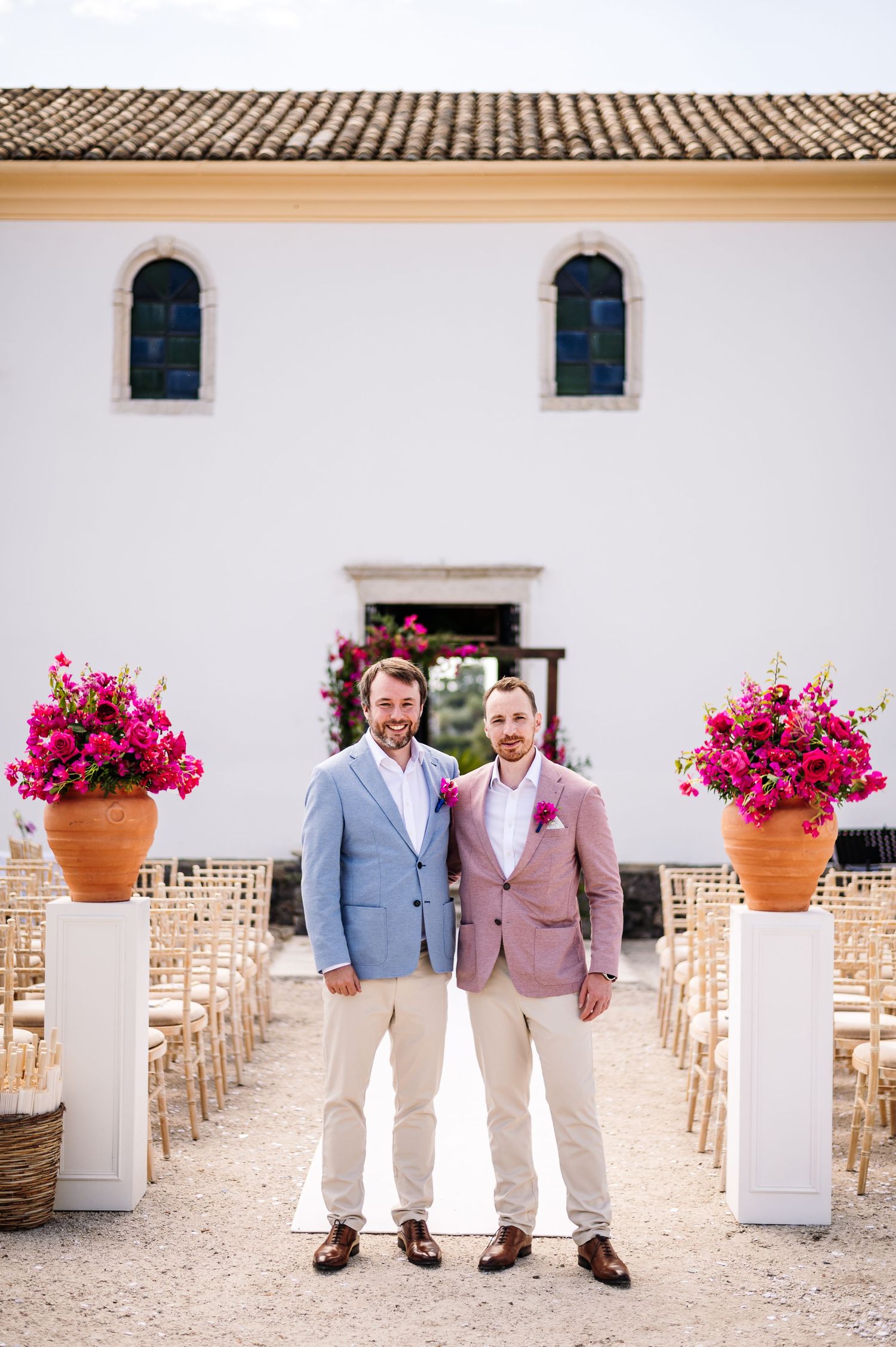 Wedding venue exterior with pink floral arrangements and rows of wooden chairs for outdoor ceremony.