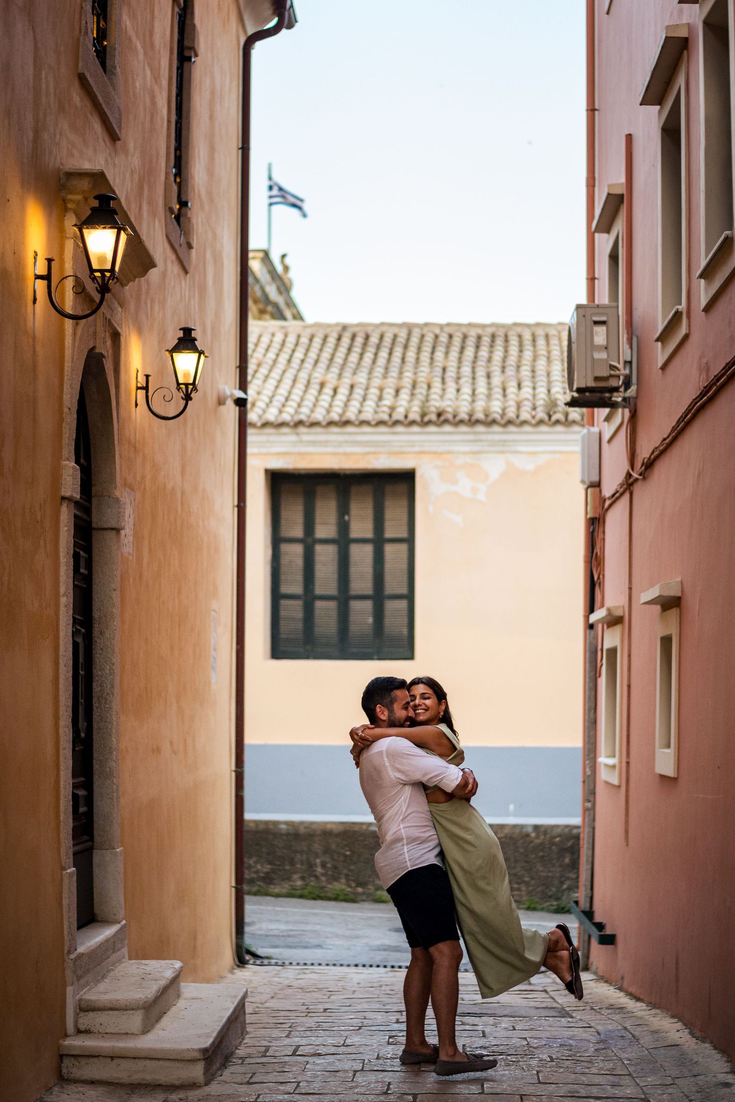 A joyful moment shared between two people in a narrow Mediterranean street with peach-colored walls.