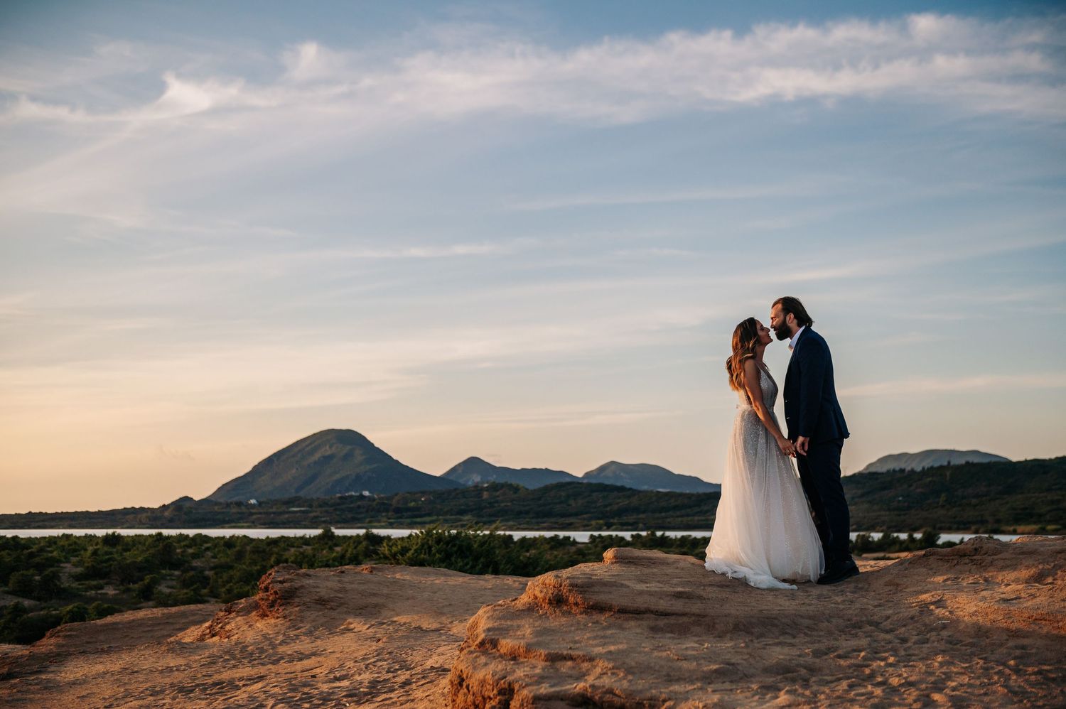 Wedding couple silhouetted against sunset sky with mountain backdrop.