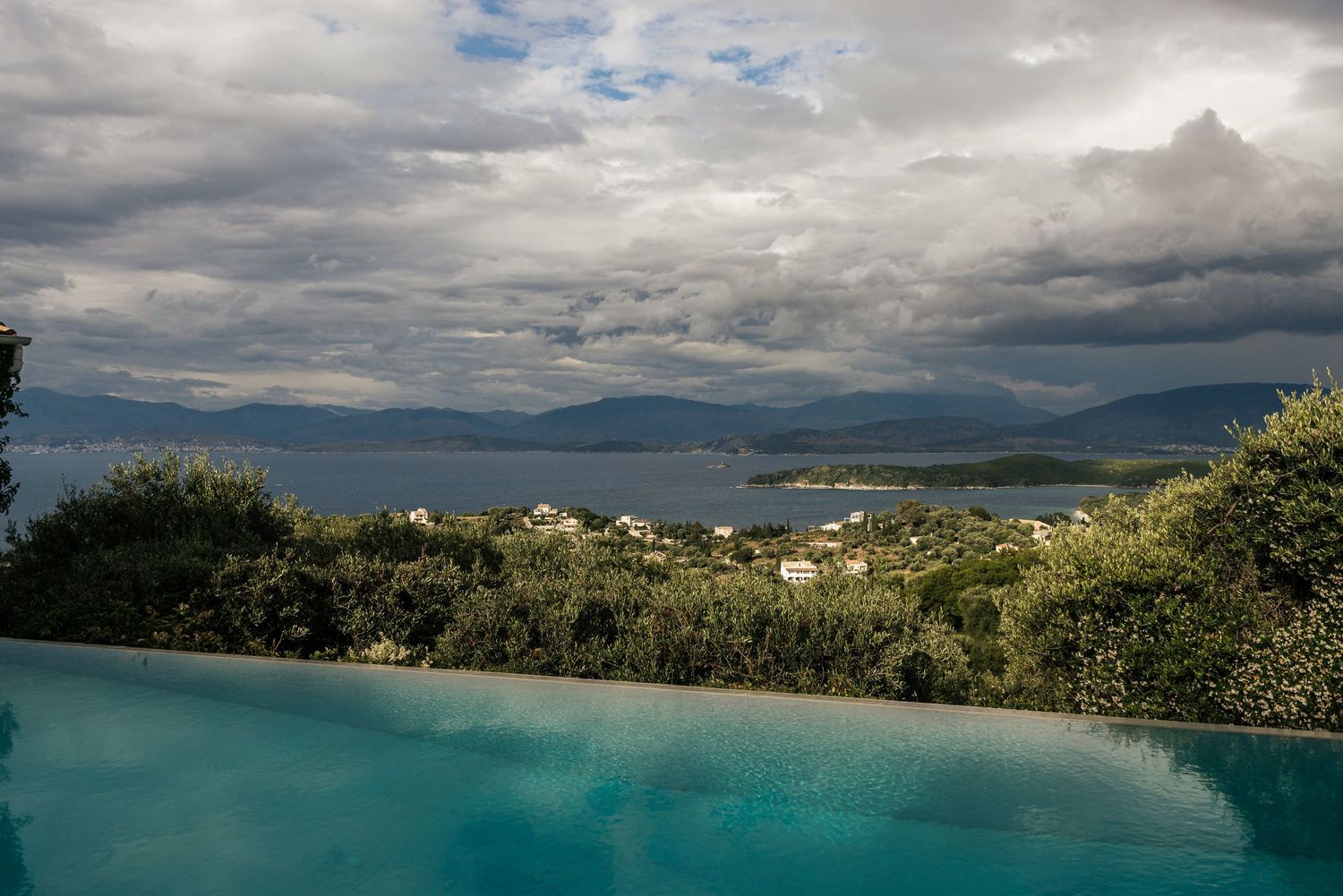 Panoramic view of a coastal landscape with mountains and blue waters under cloudy skies.