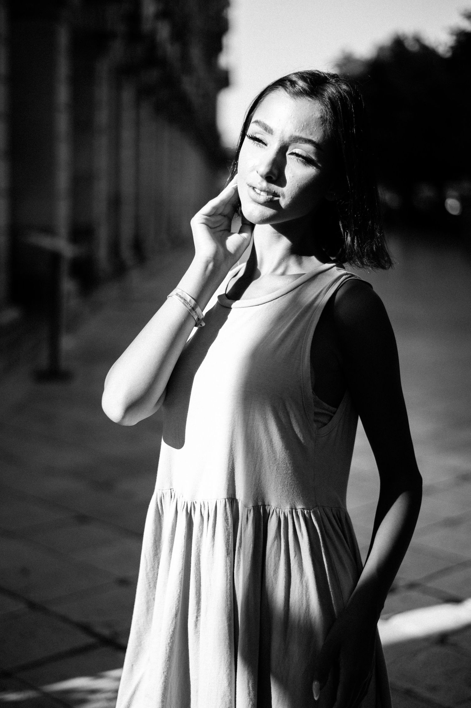 Black and white portrait of a woman in a flowing dress posing on a city street.