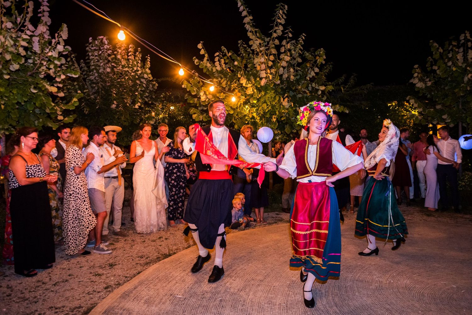 Wedding guests dance together at an outdoor evening reception under string lights.