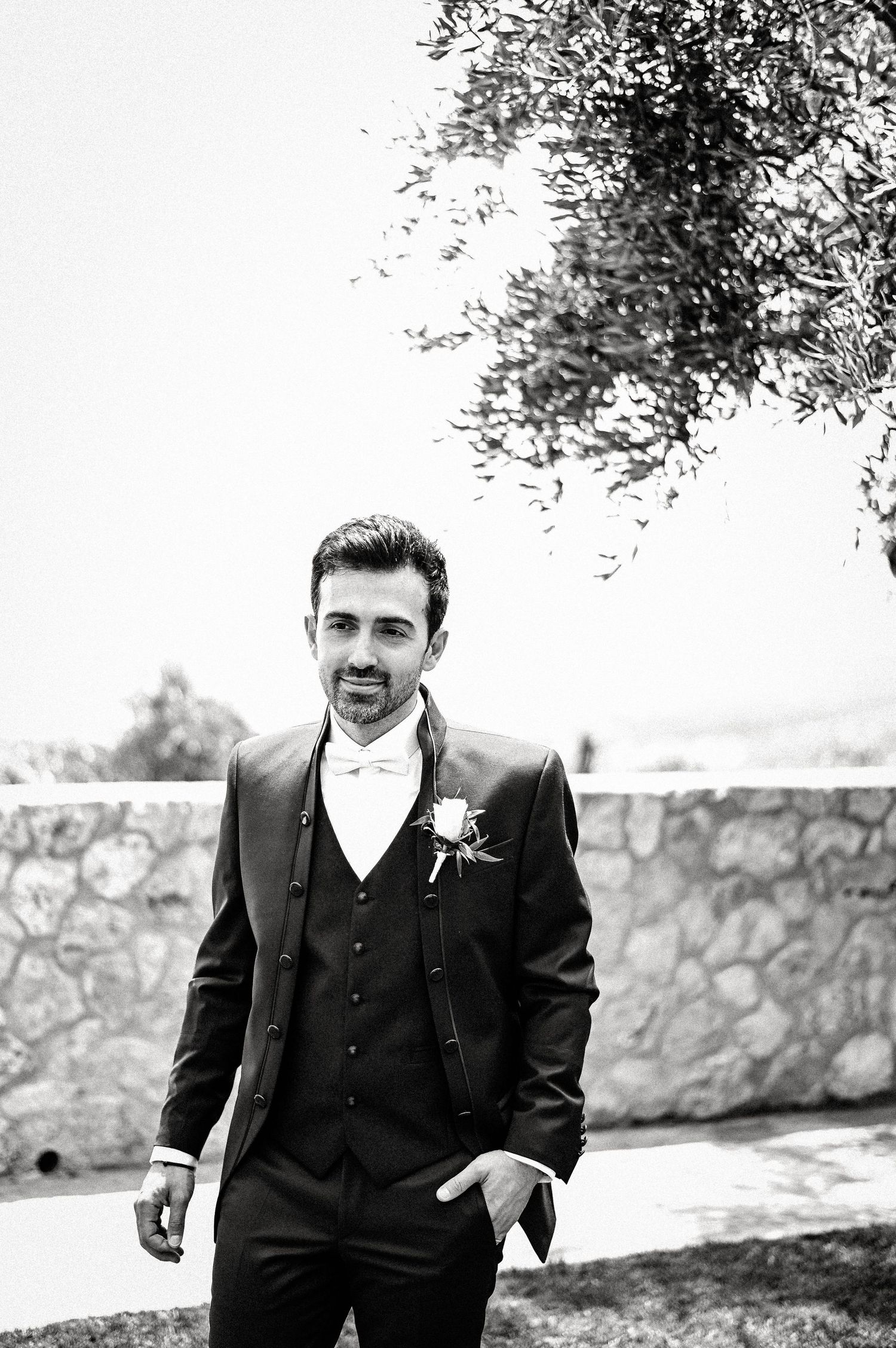 Black and white outdoor portraits of groom in formal attire against stone wall.