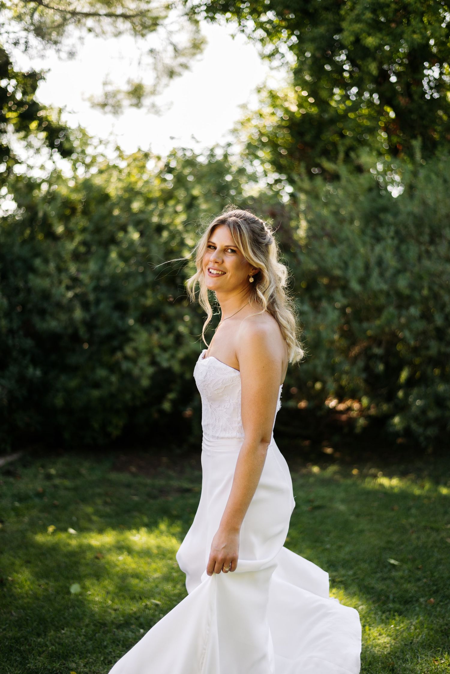 A bride in a white wedding dress twirls joyfully in a sunlit garden setting.