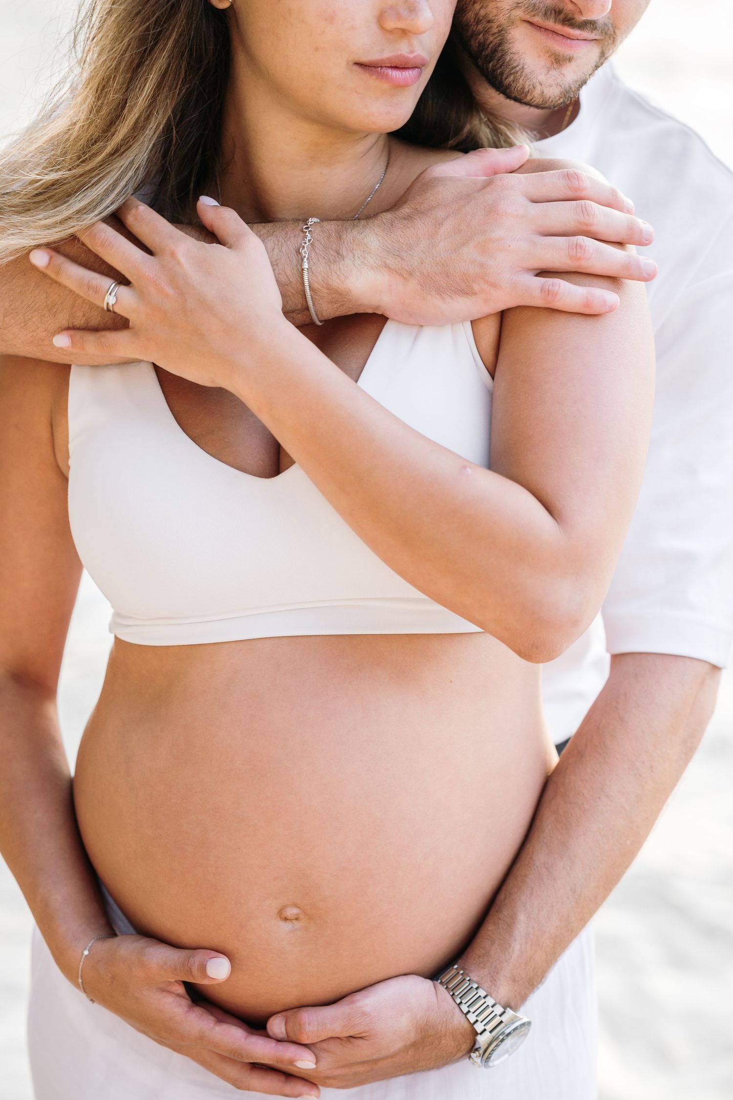 Intimate close-up of embrace in white clothing against bright background.