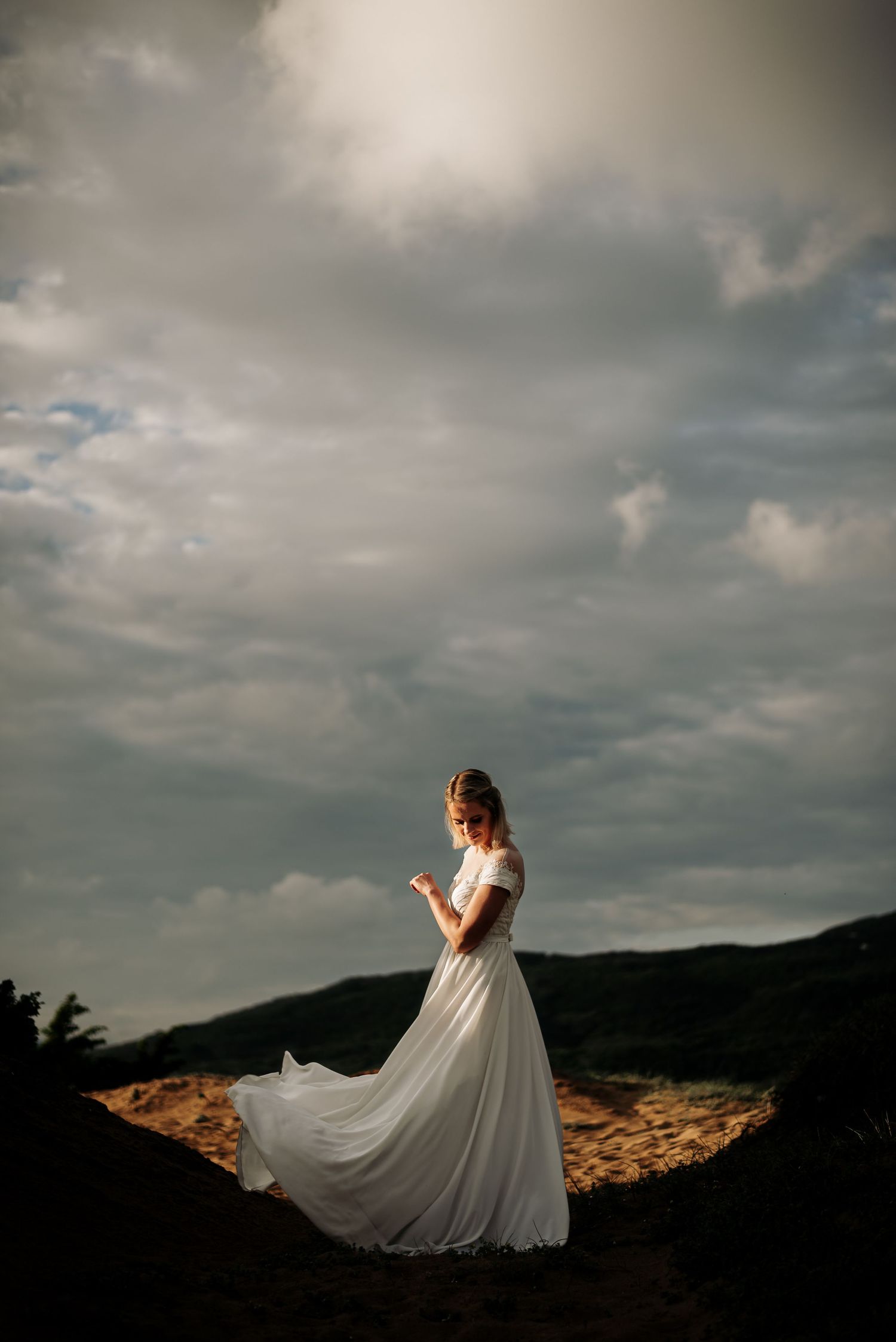 Wedding dress flowing dramatically against stormy mountain landscape.