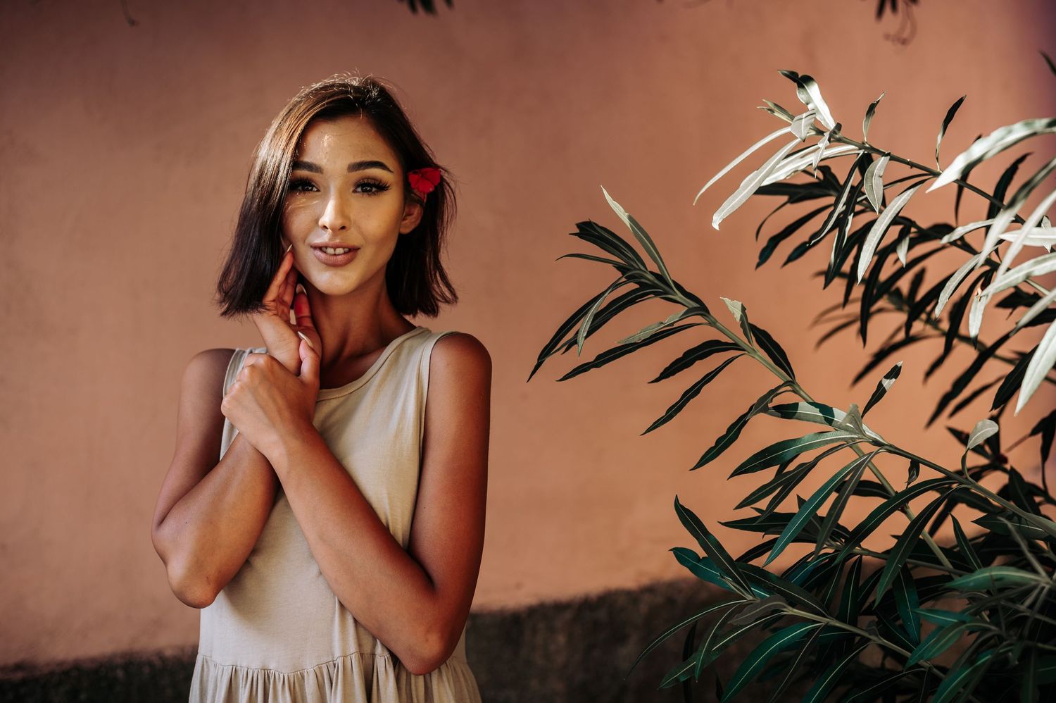 Woman in flowing dress posing among tropical plants with warm sunset lighting.