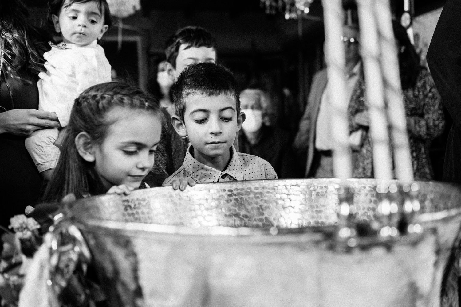 Children peer curiously into a baptismal font during a religious ceremony.