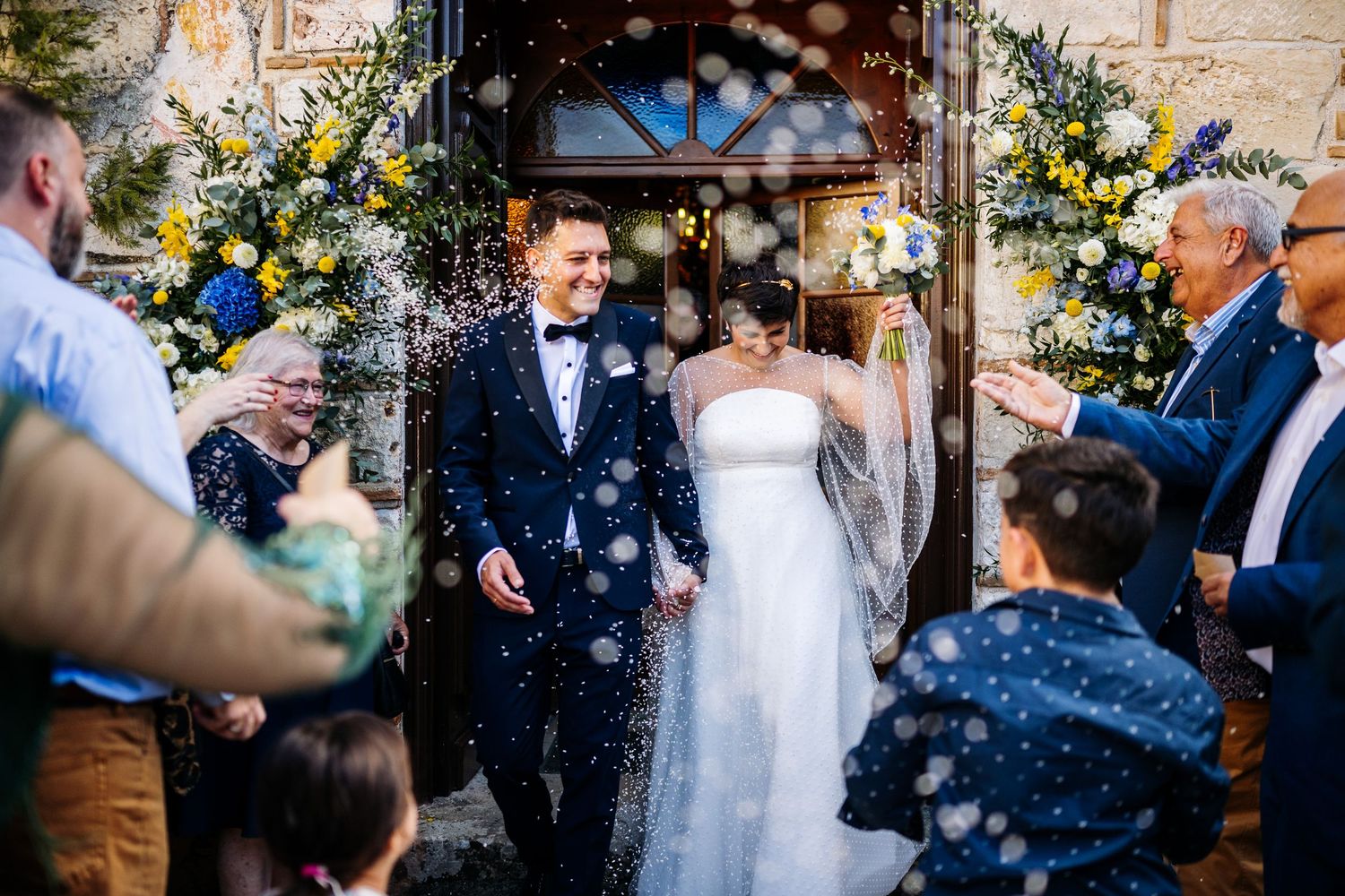 Wedding guests throwing confetti outside a stone church building in celebration.