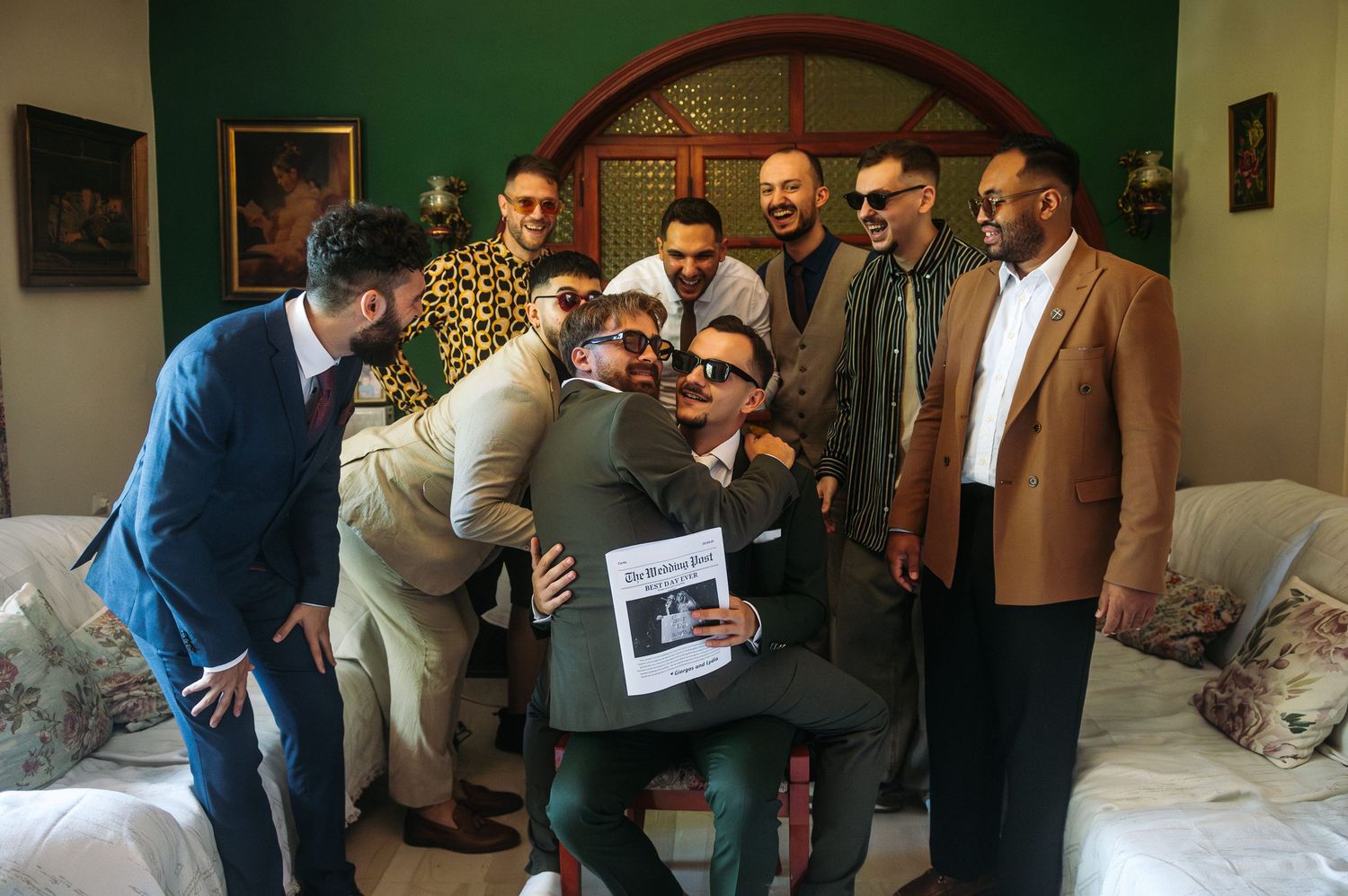 A group of formally dressed guests gather in a room with green walls for a wedding event.