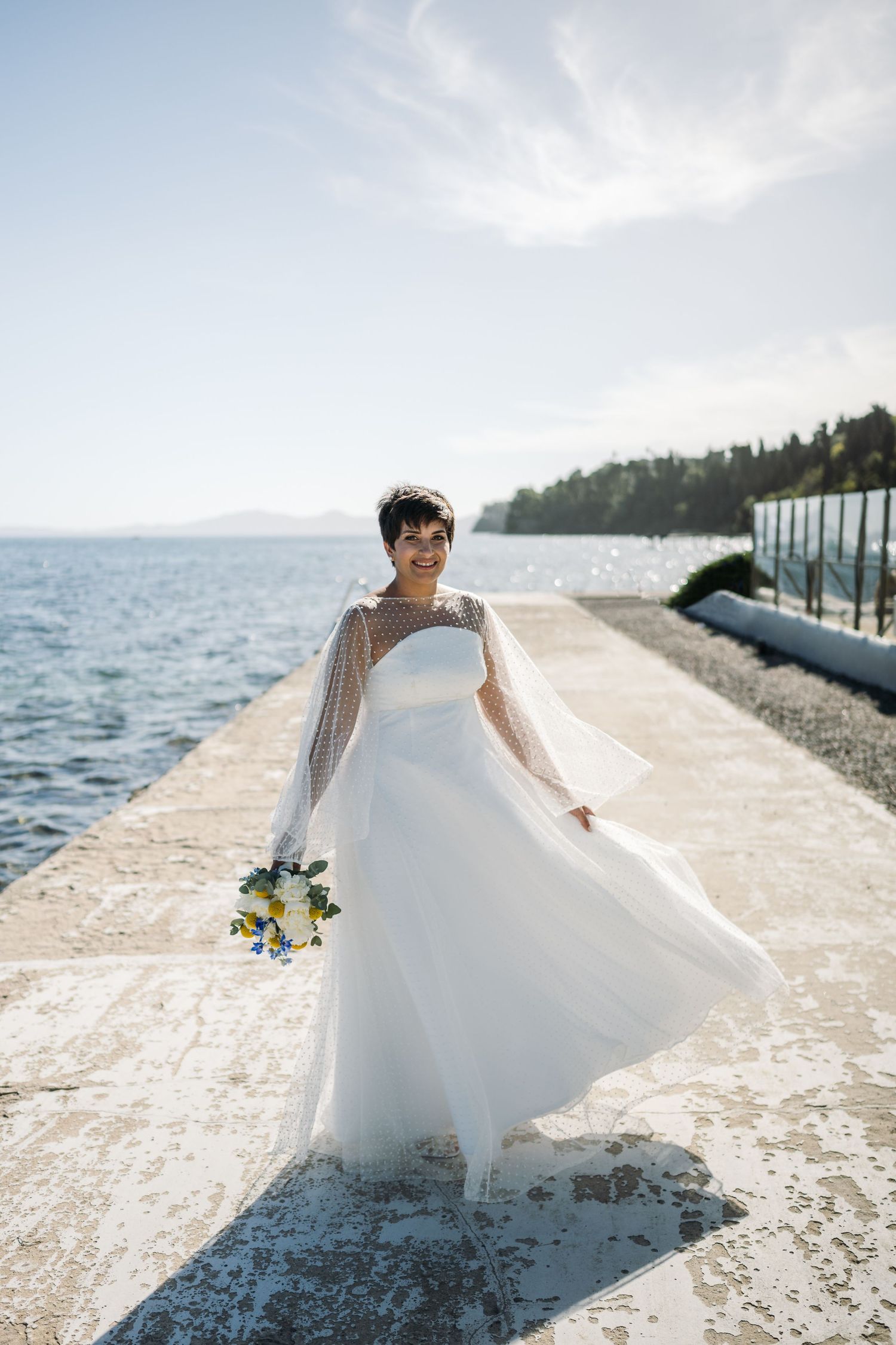 An elegant bridal dress spins in motion against a waterfront backdrop on a sunny day.