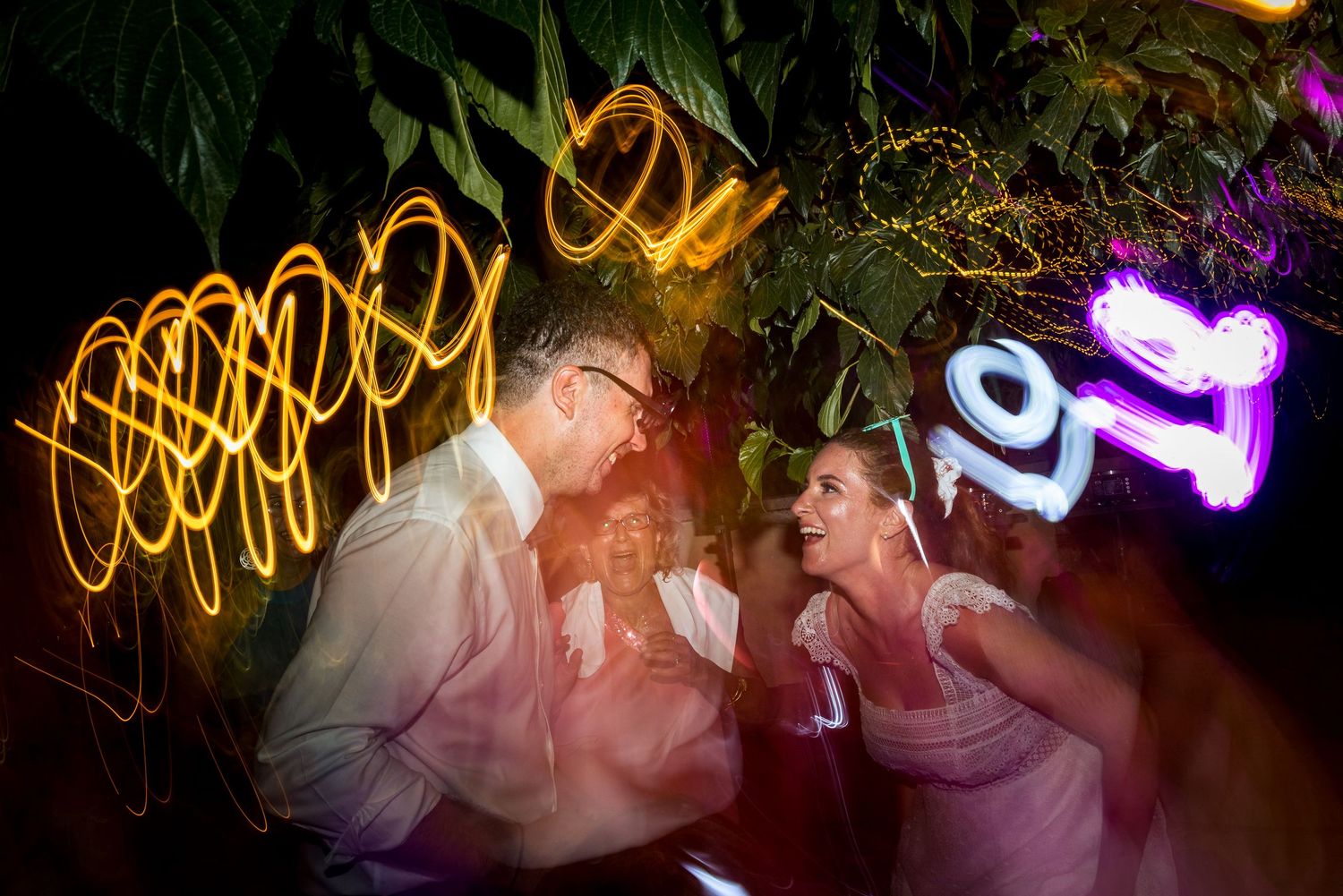 Colorful light trails and bokeh effects create an artistic nighttime wedding photography scene.