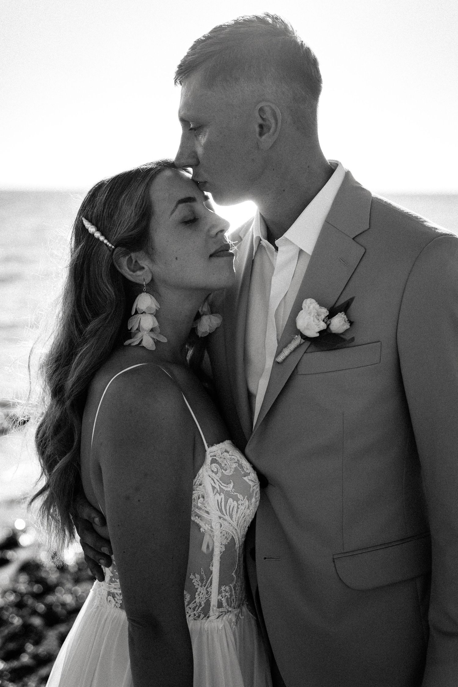 A romantic black and white wedding portrait showing a tender moment between newlyweds by the ocean.