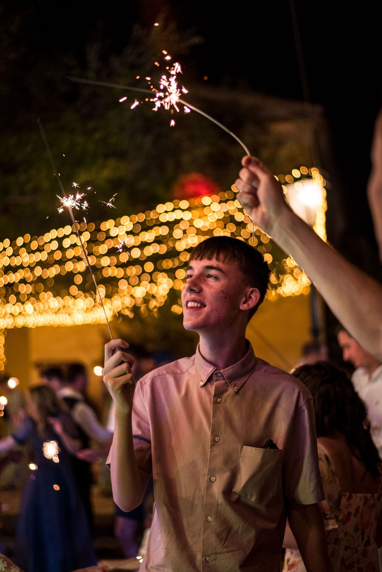 Guest enjoying sparklers at outdoor evening celebration with twinkle lights in background.