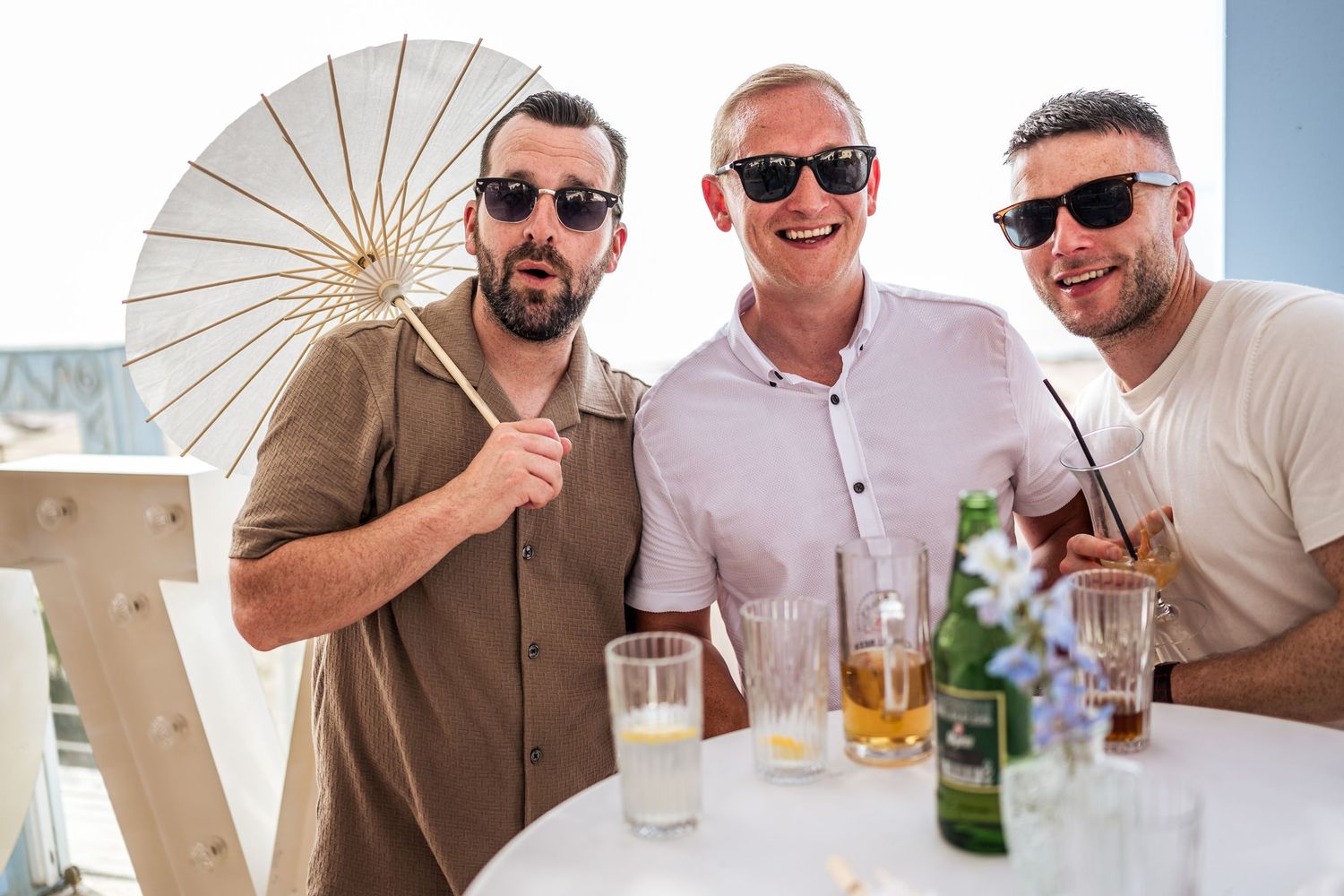 Group of friends enjoying drinks under white parasols at a beachside gathering.