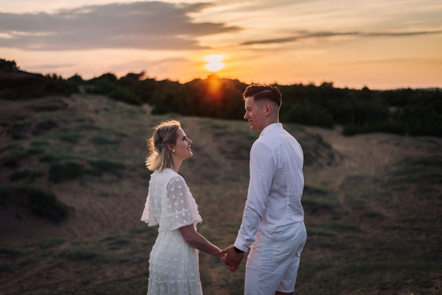 Couple holding hands while watching a golden sunset over rolling hills.