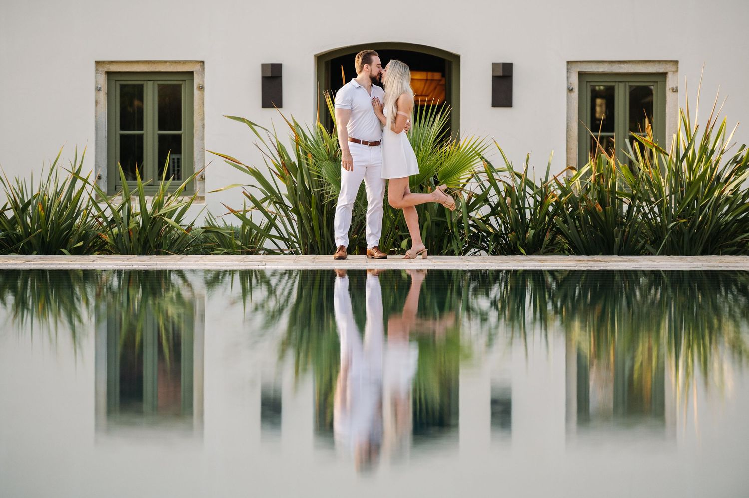A couple strolls together on a white stone pathway next to a reflective pool.