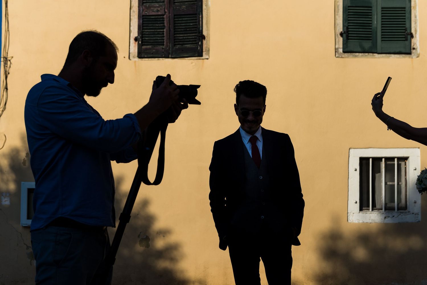 Silhouettes of wedding guests against a yellow wall creating dramatic shadows and shapes.