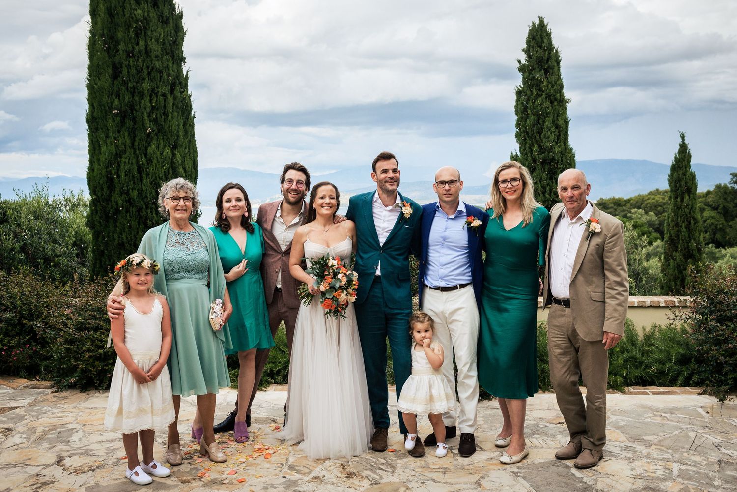 Wedding party gathered for a group photo against a scenic countryside backdrop.