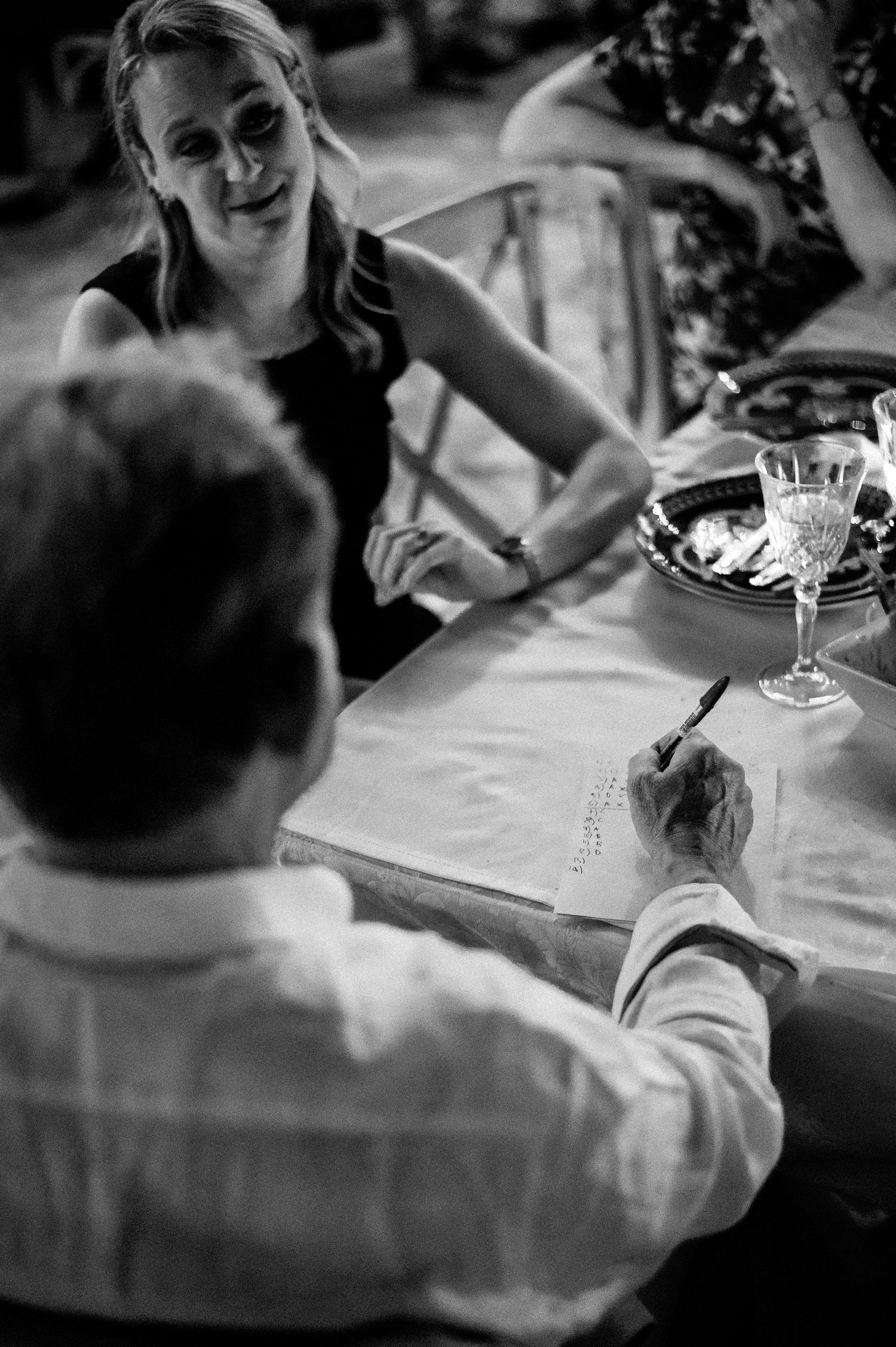 Black and white image of wedding guests seated at reception tables with wine glasses.