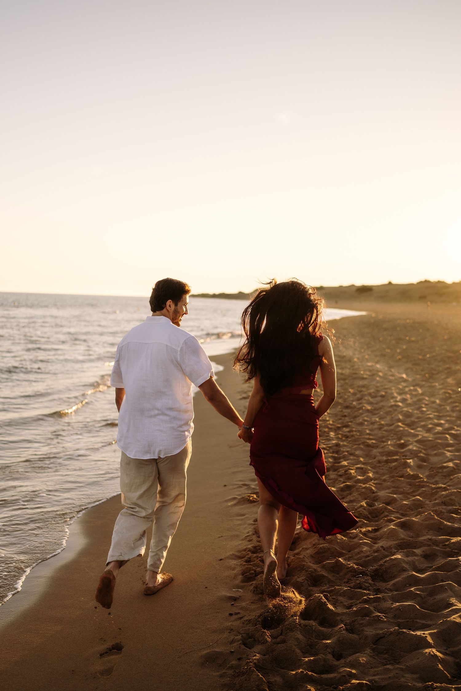 Romantic couple strolling along the shoreline during golden hour.