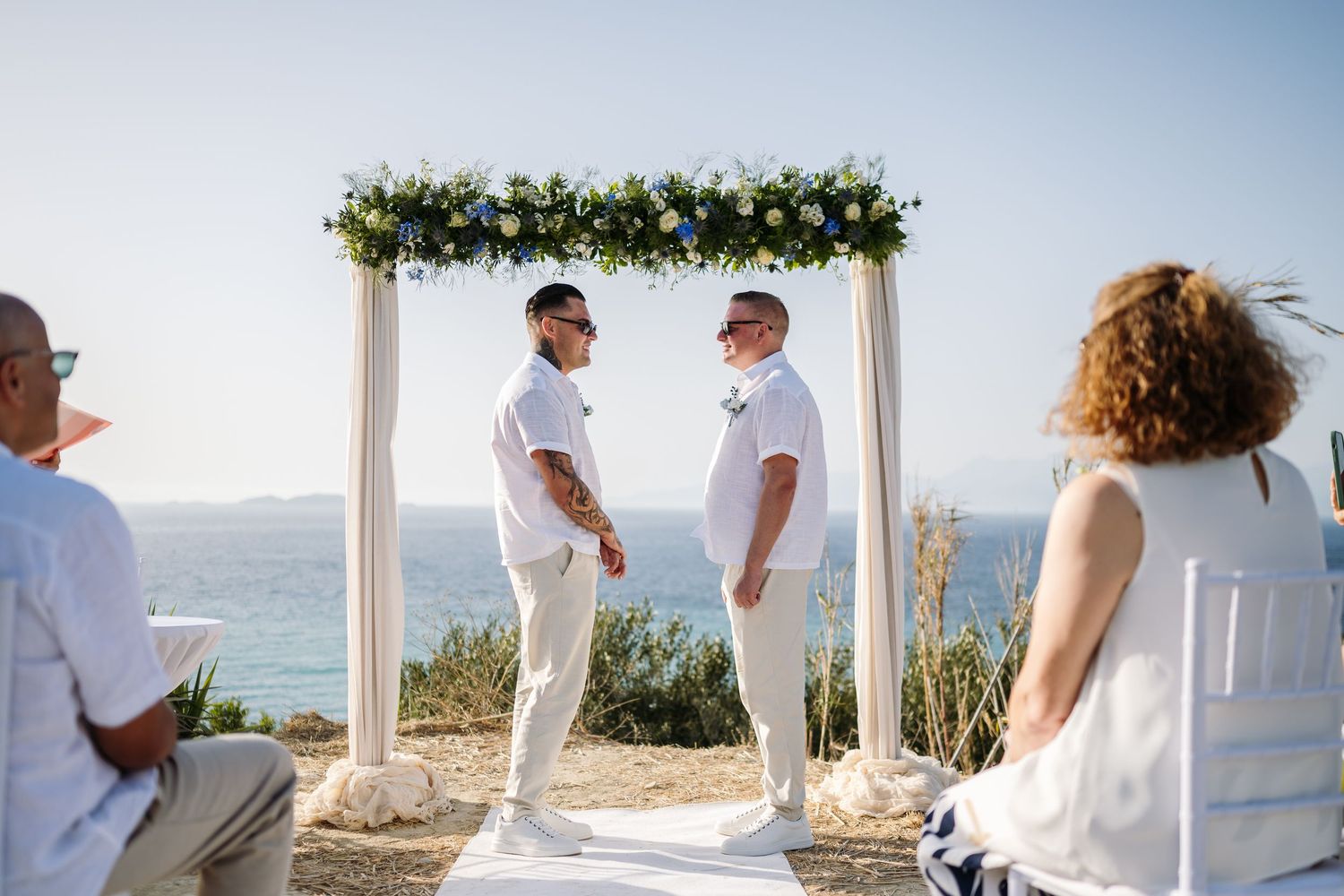 Beachside wedding setup with white arch and chairs against a stunning ocean backdrop.