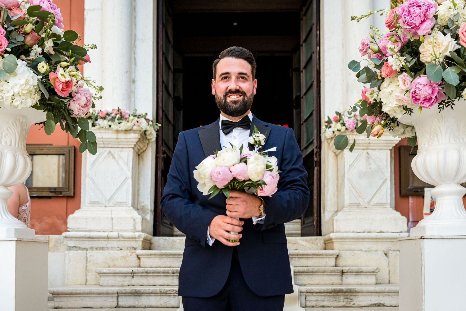 Wedding party posing with floral arrangements and decorative urns in an elegant outdoor setting.