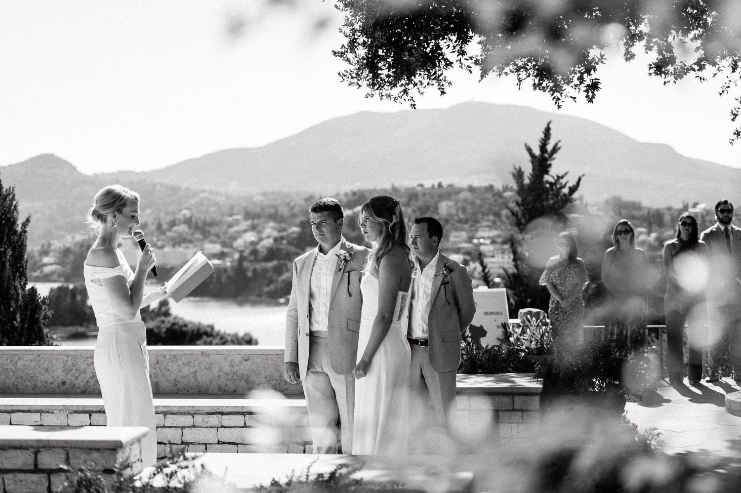 Wedding ceremony guests in soft focus with mountain landscape backdrop.