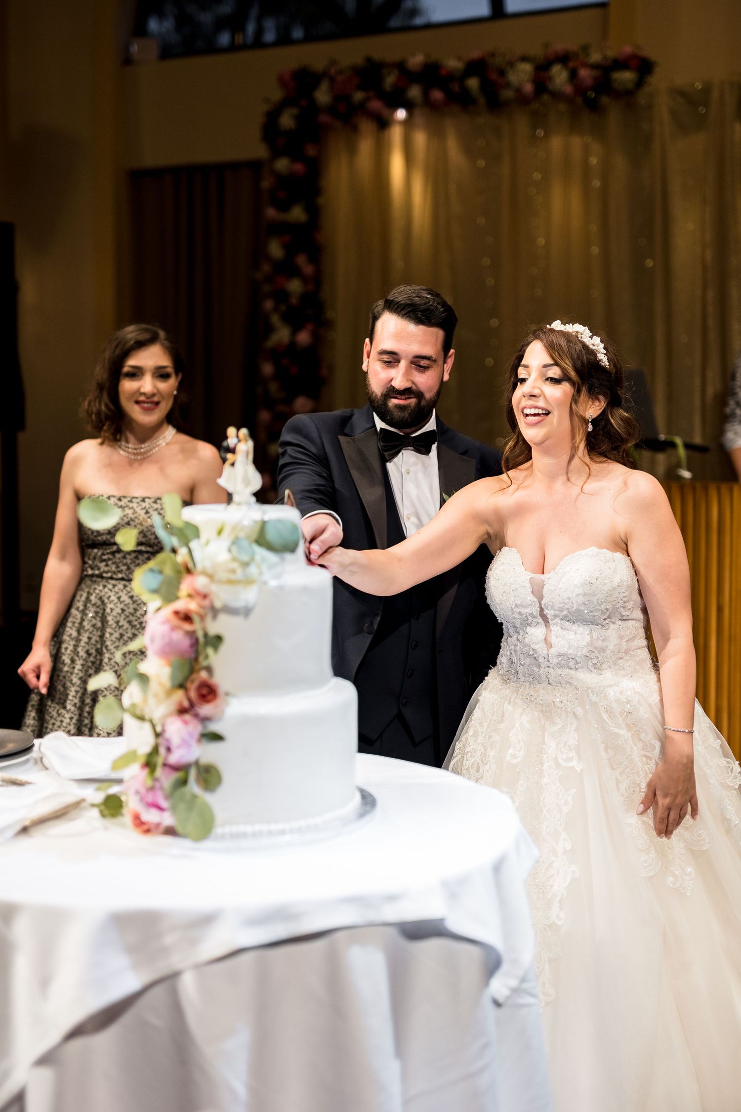Wedding couple cuts their elegant white tiered cake decorated with fresh flowers.