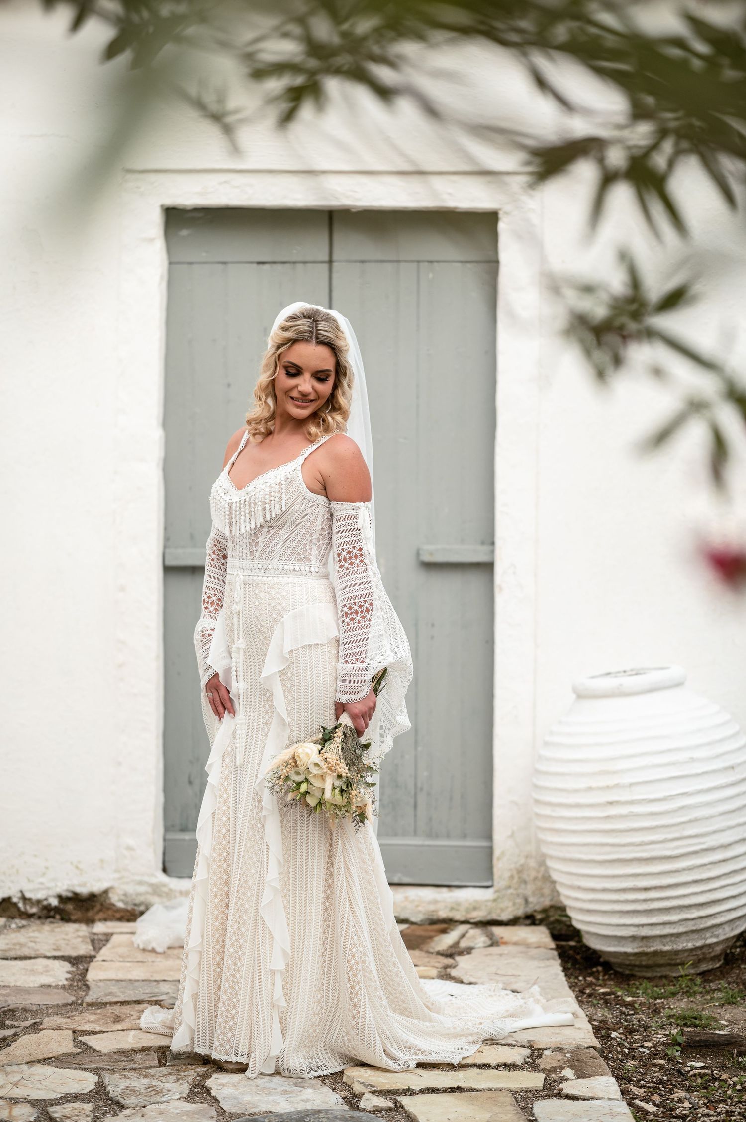 Bride in bohemian lace dress poses against white wall with paper lanterns.