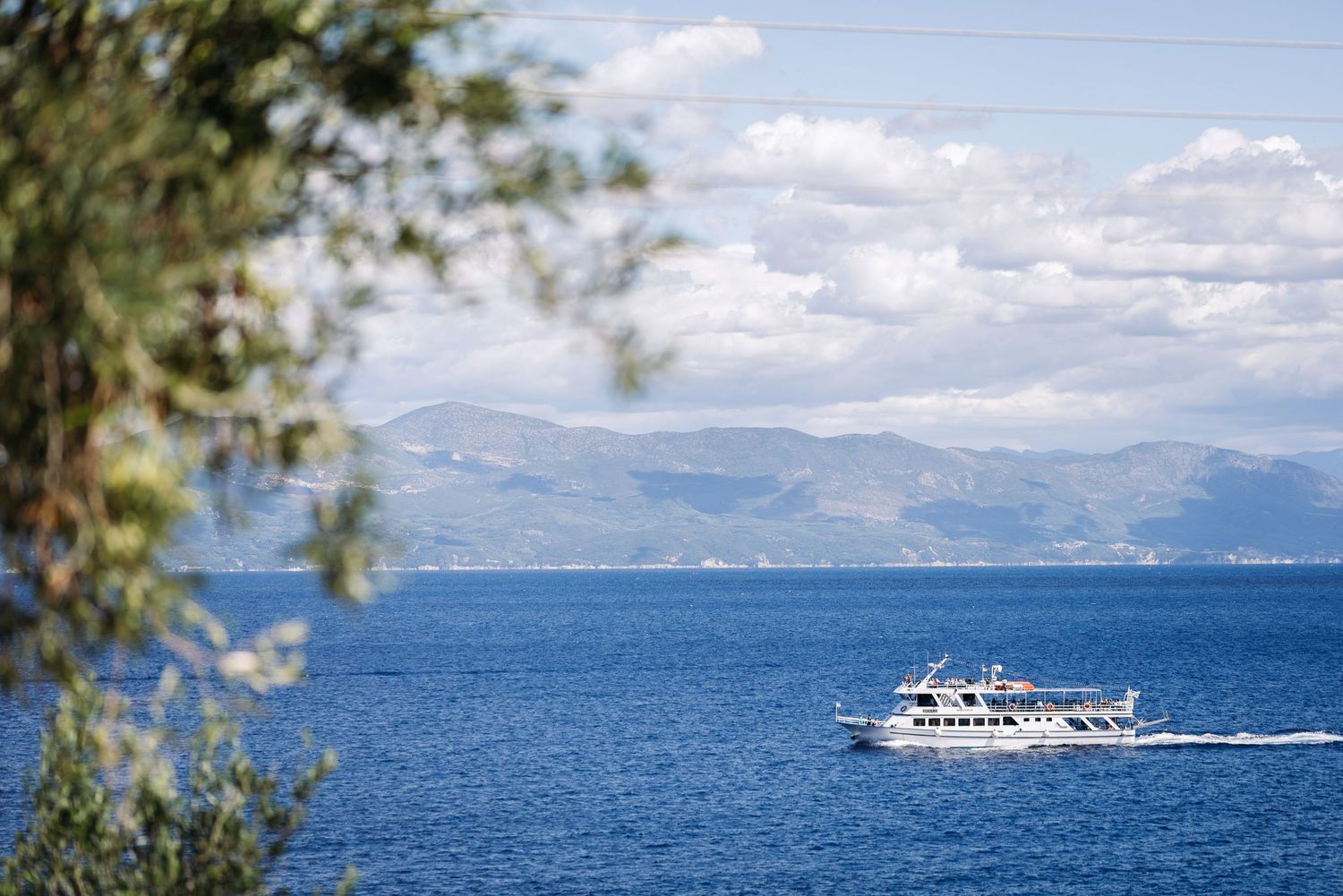 Passenger ferry boat cruising on blue Mediterranean waters with mountains in background.