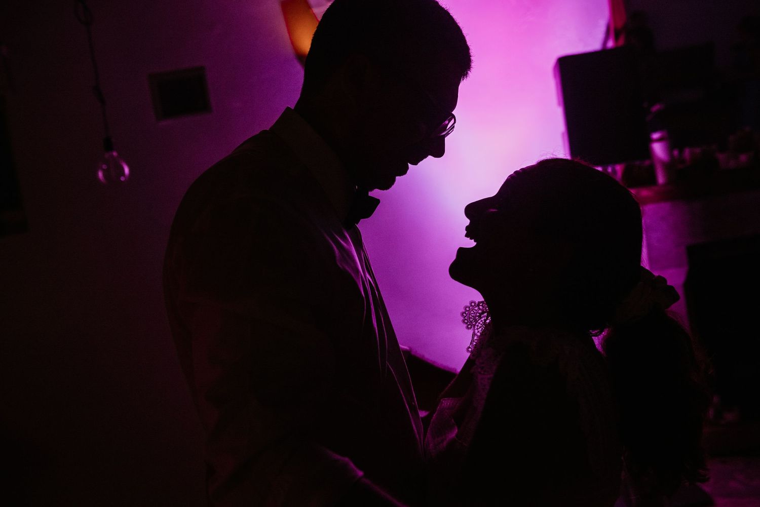 Silhouettes of party guests dancing against purple lighting at an evening celebration.