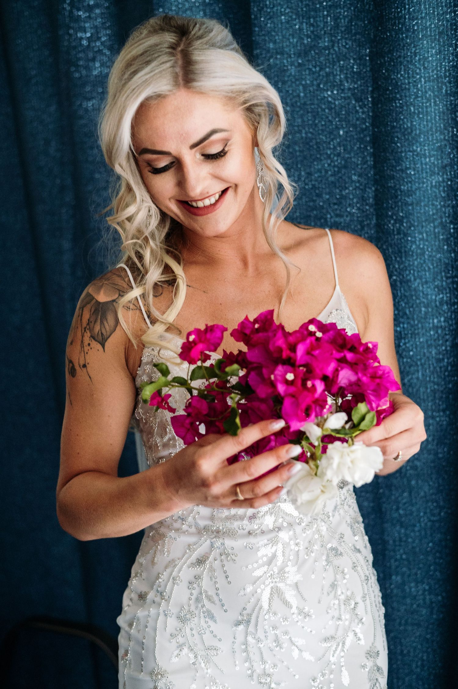 Bride holding vibrant pink and white flowers against a lace wedding dress and blue backdrop.