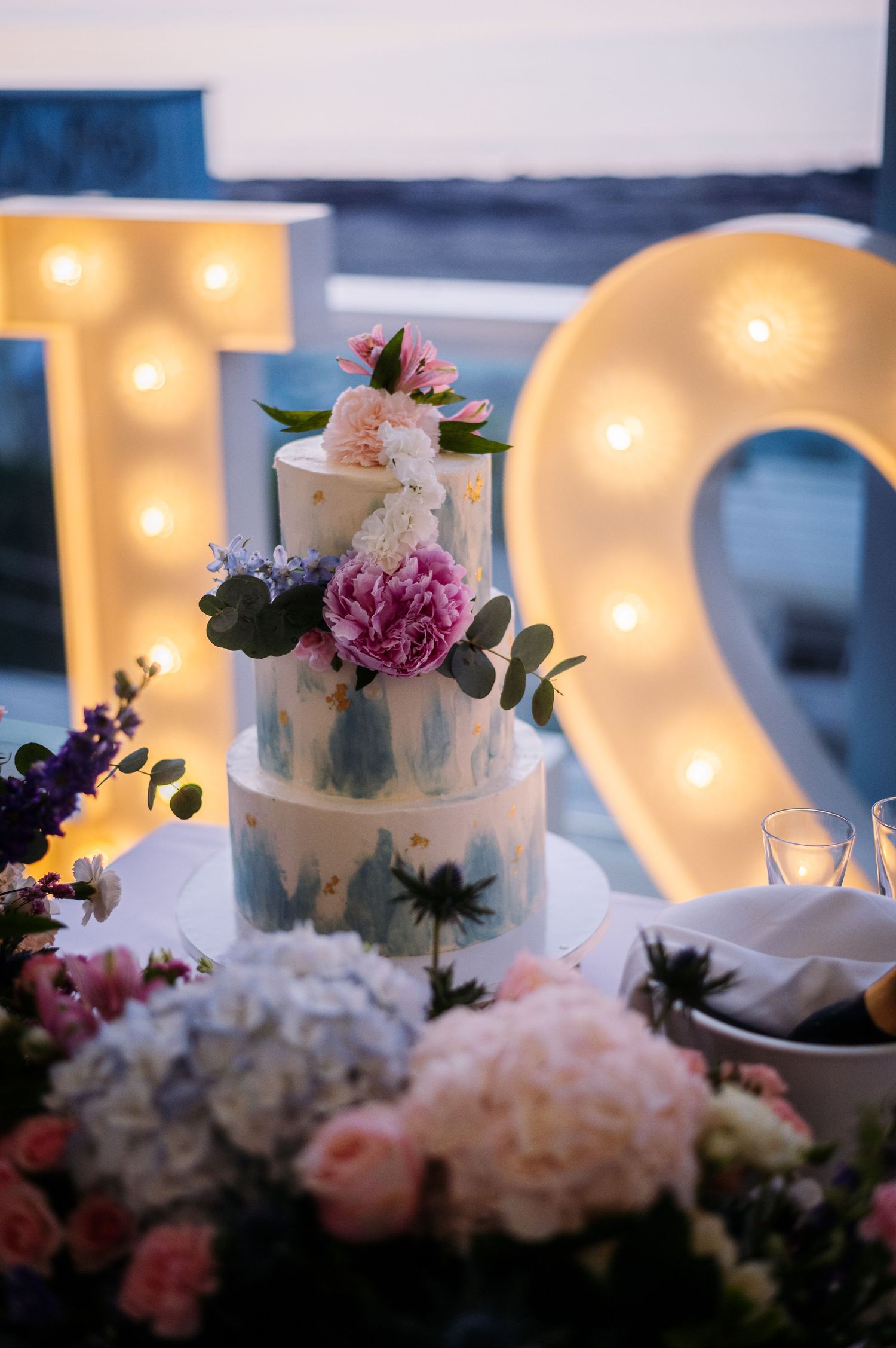 Wedding cake and floral decorations with illuminated LOVE sign in background.