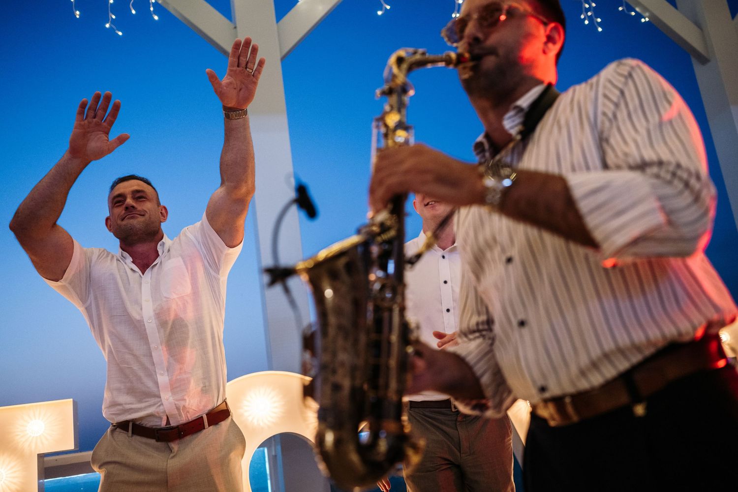 Wedding party dancing and celebrating under twinkling lights at outdoor reception.