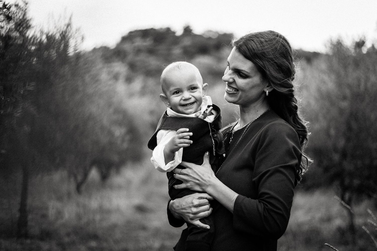 A black and white portrait of a baby being held outdoors against a natural background.